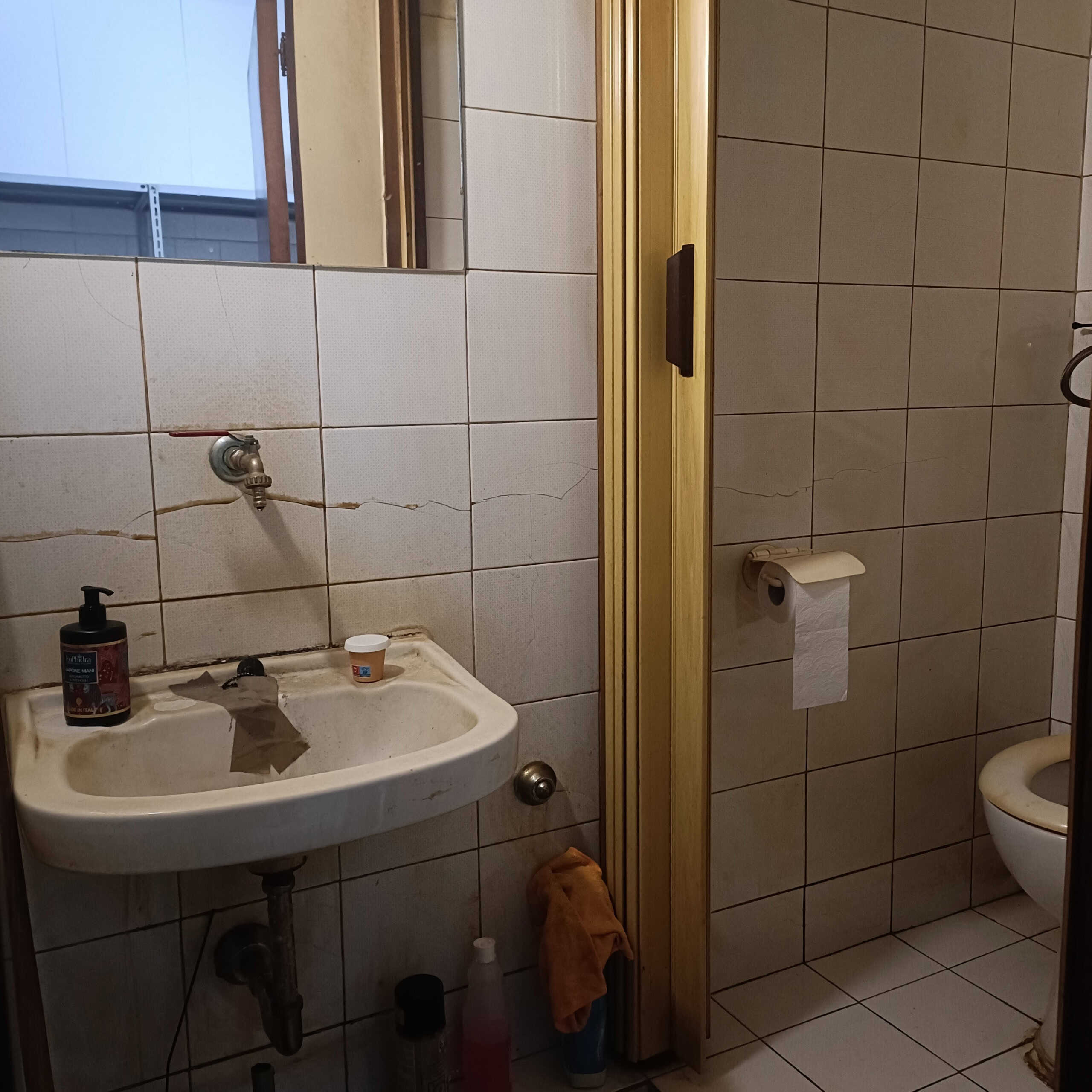 Lavandino e toilette vecchi con piastrelle rotte in bagno singolo, ambiente da ristrutturare, elementi di arredo semplici e anticati, nextcasa.it.
