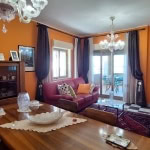Elegante soggiorno con pareti arancioni, divani in pelle rossa, candelabri, mobili in legno, tappeti e finestre ampie, ambiente accogliente e ben arredato.