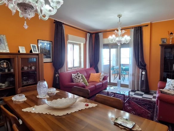 Elegante soggiorno con pareti arancioni, divani in pelle rossa, candelabri, mobili in legno, tappeti e finestre ampie, ambiente accogliente e ben arredato.