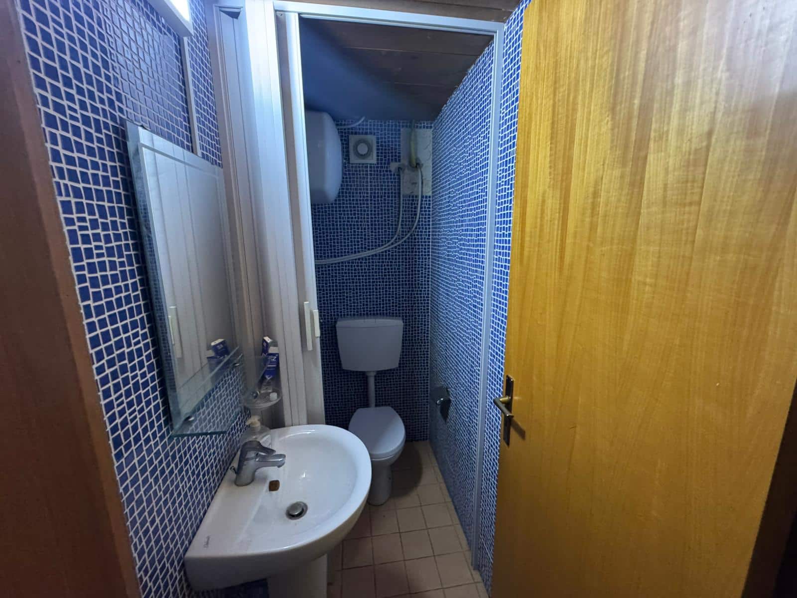 Prodotto bagno con piastrelle blu, lavabo, water e doccia, ideale per affitti brevi o uso quotidiano in strutture ricettive e abitazioni private. Nexus tra funzionalità e praticità in un ambiente compatto.