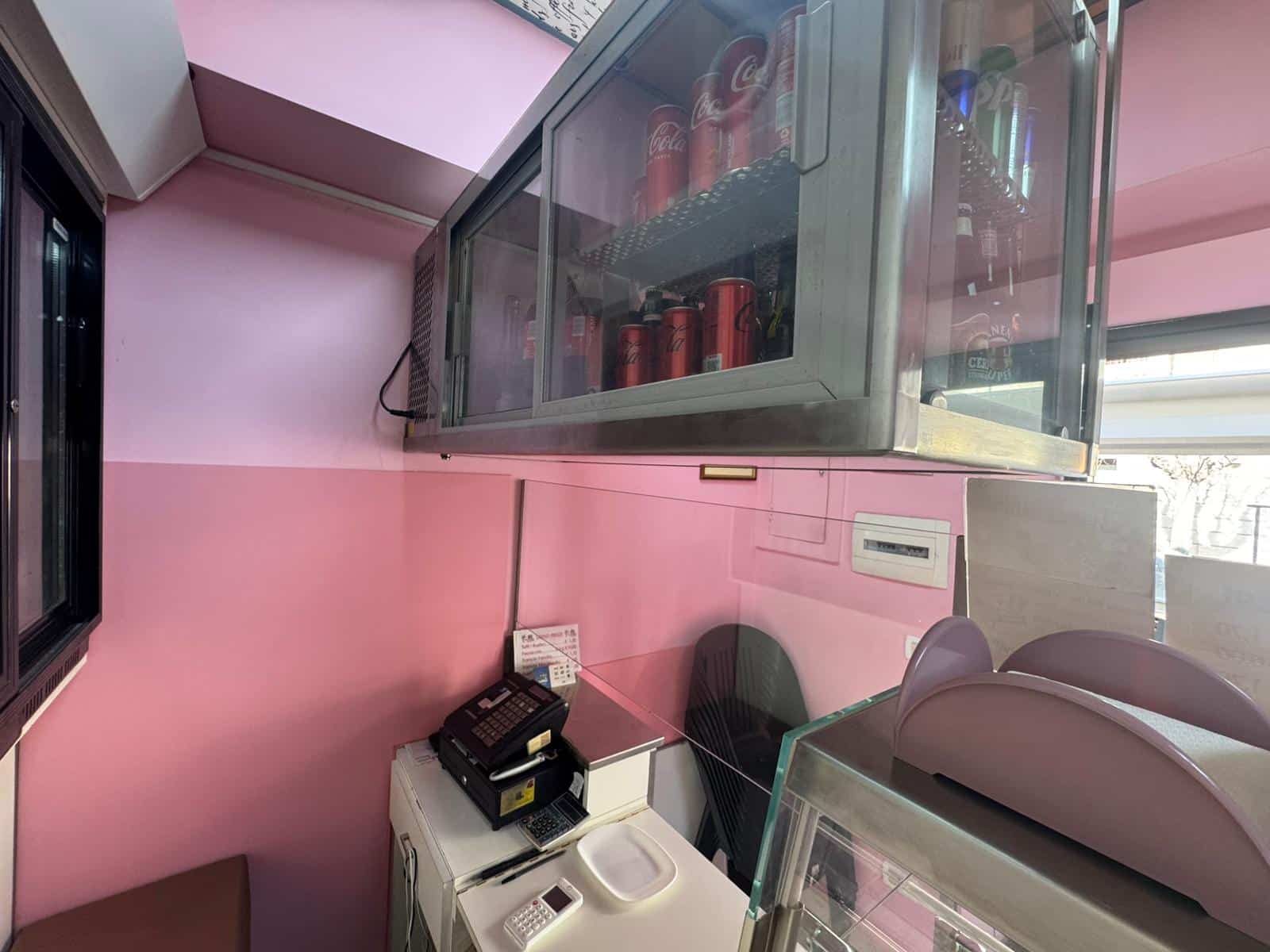Birreria con frigorifero refrigerato, arredamento rosa e bancone con sedie, spazio commerciale ben organizzato, ambiente accogliente e moderno, ideale per attività di ristorazione e vendita di bevande.