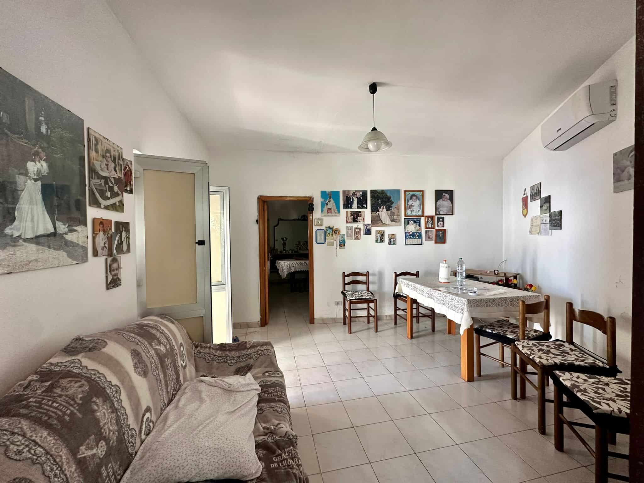 Soggiorno spazioso con pareti decorate con foto e quadri, arredato con divano e tavolo con sedie, ambiente luminoso e accogliente, ideale per famiglie o incontri conviviali, perfetto per scoprire le proposte immobiliari di NextCasa in Italia.