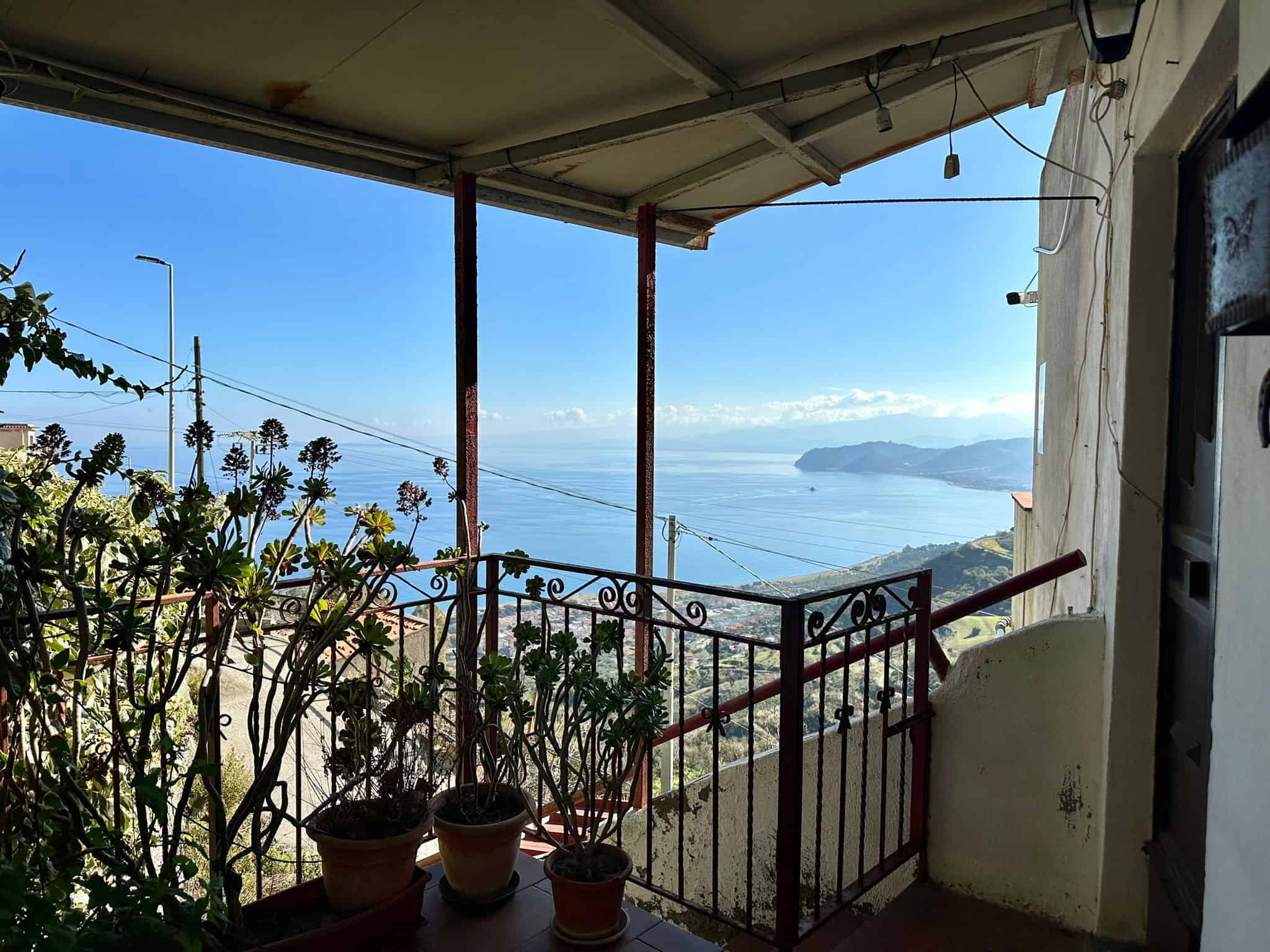 Vista mare e costa in balcone con piante e ringhiera in ferro battuto in immobile vicino al mare, zona panoramica, casa con terrazza.