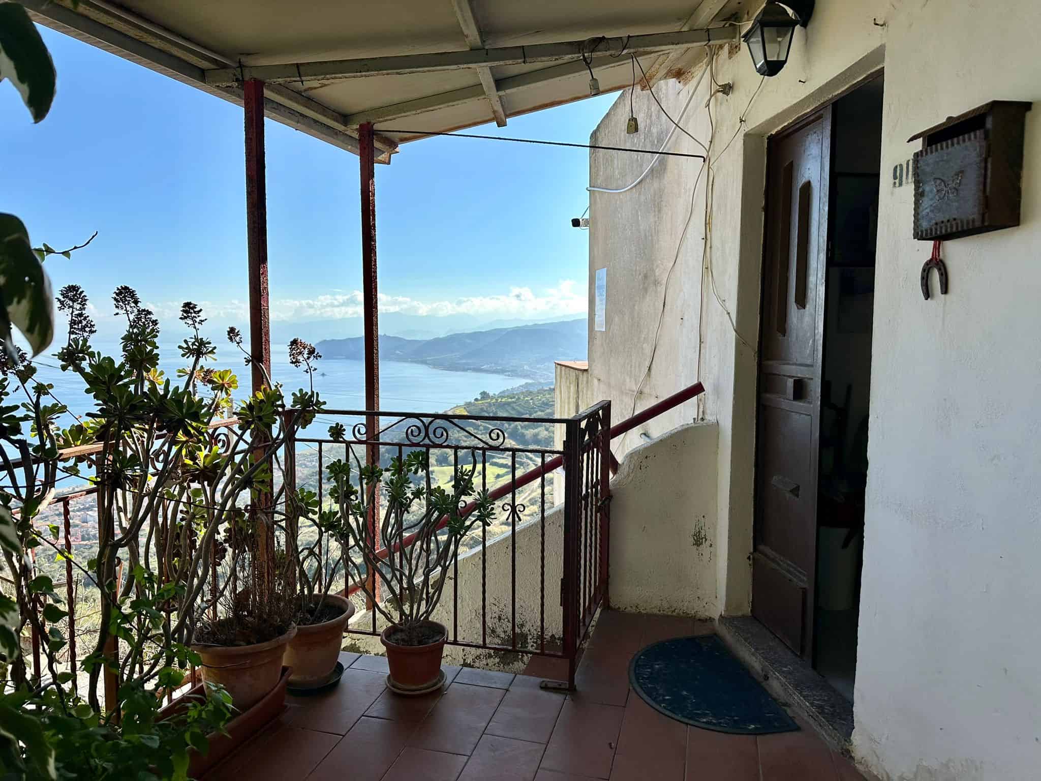 Vista panoramica dal balcone di un appartamento con piante ornamentali e vista sul lago e le montagne, in una zona tranquilla e immersa nella natura.