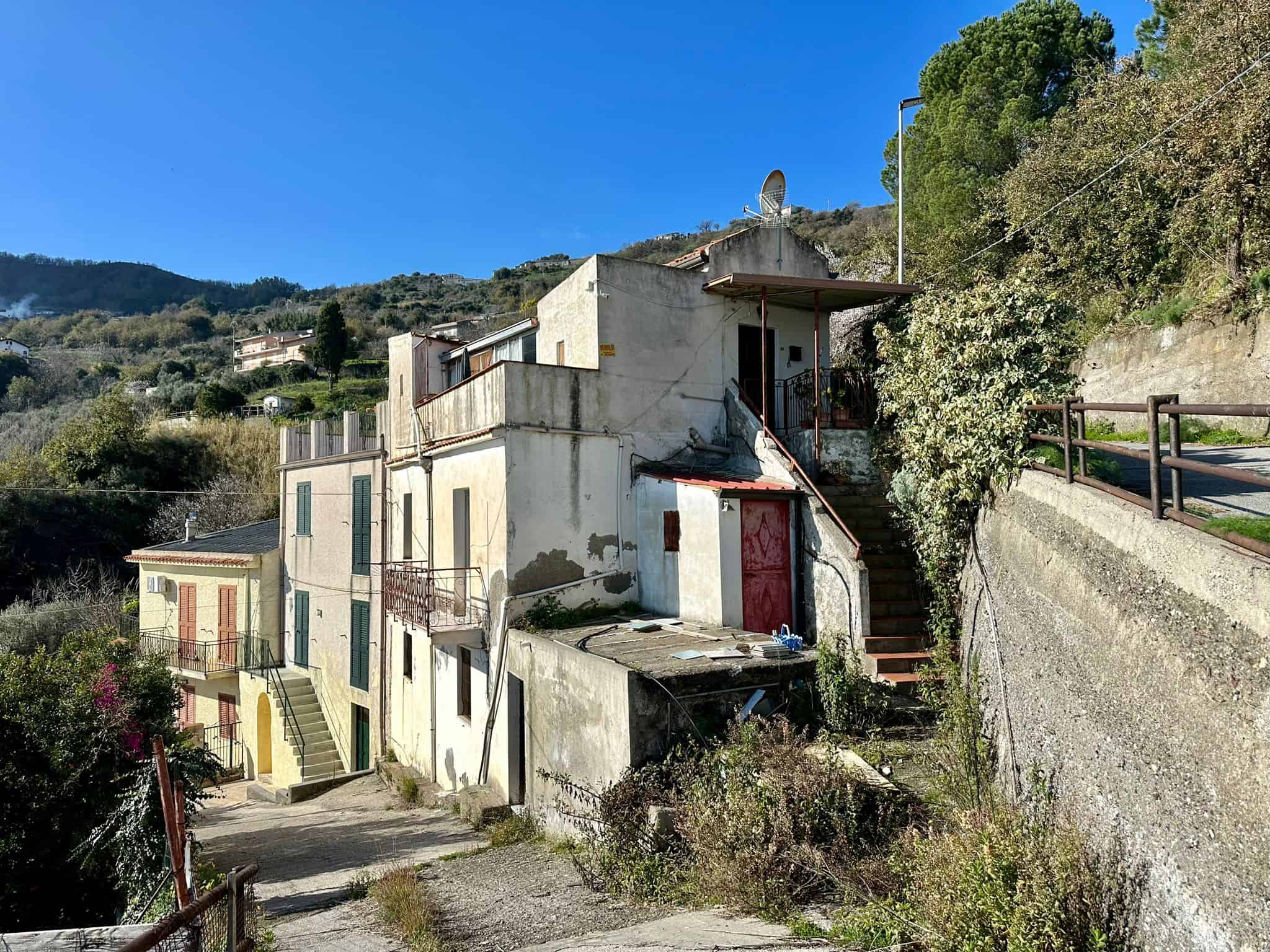 Casale rustico in zona collinare con vista su case tradizionali e natura, immerso nel verde. Ideale per ristrutturazione e progetti di investimento immobiliare. Prospetti esterni e accesso pedonale in ambiente tranquillo e suggestivo.