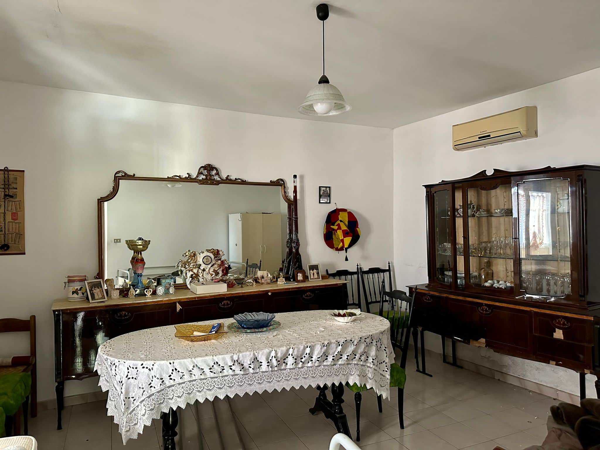 Antico soggiorno con tavolo da pranzo, mobile con specchio e oggetti d'antiquariato, ambiente elegante e accogliente, ideale per case sofisticate e storiche.