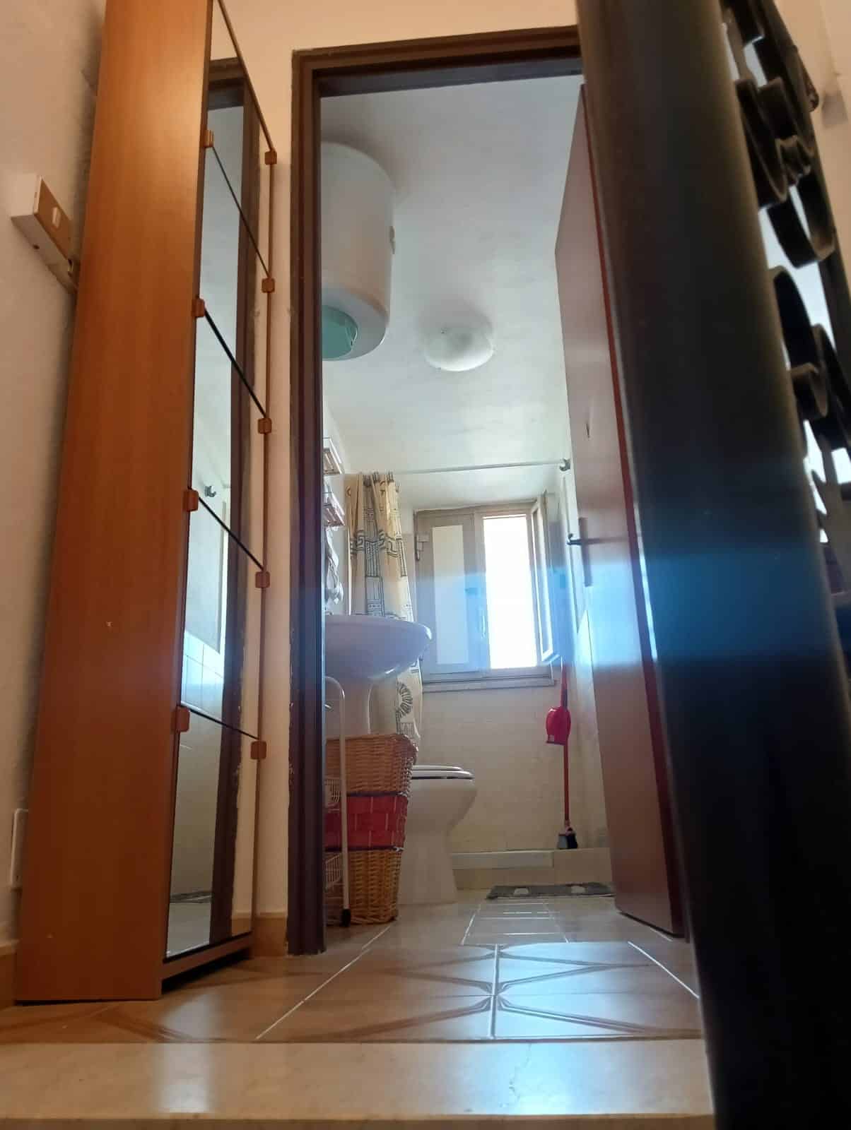Pannello di specchi nel soggiorno, vista sulla zona bagno con lavabo e finestra, arredi funzionali, pavimento in piastrelle, ambienti luminosi e accoglienti, ideale per soluzioni di arredo casa NextCasa.