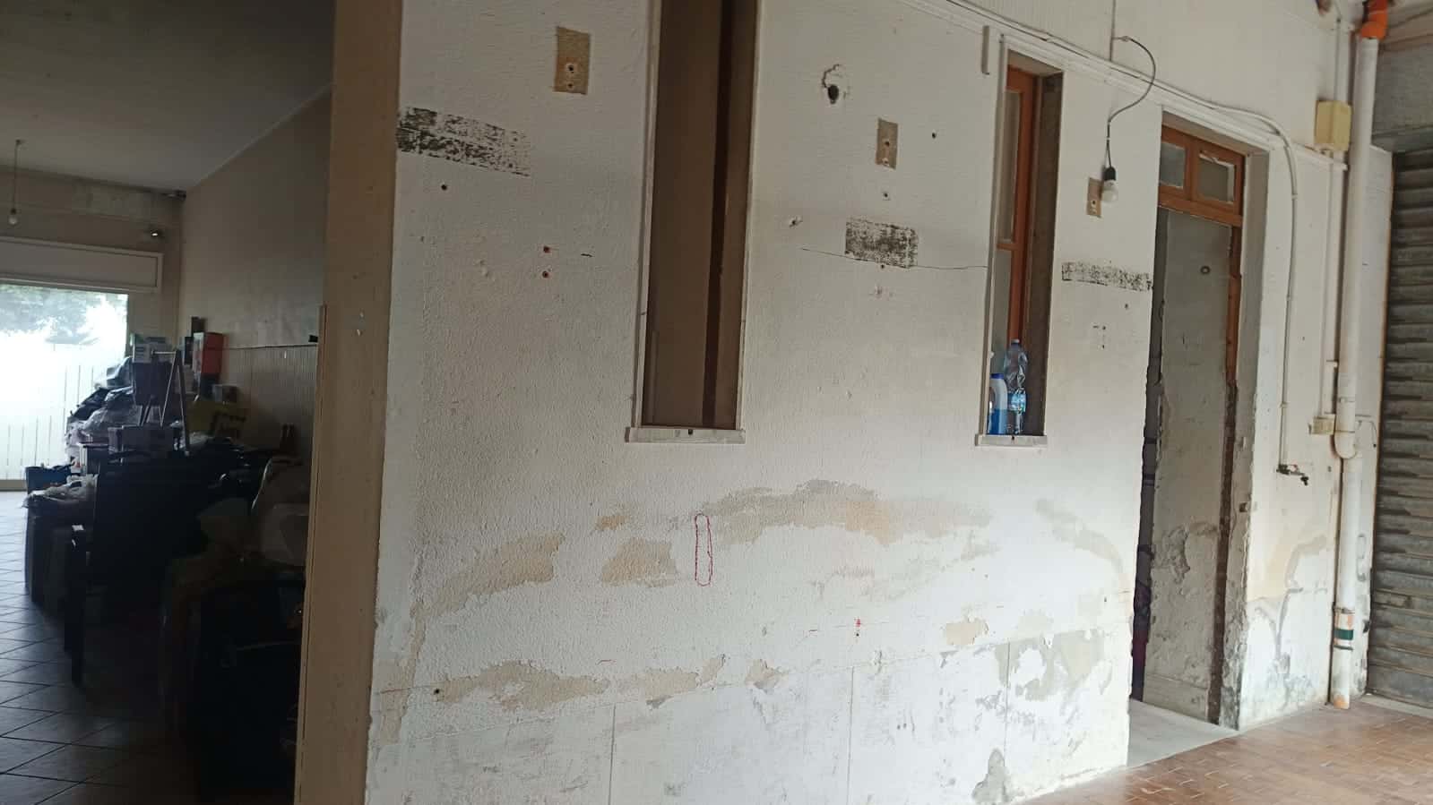 Fondo di muratura in fase di ristrutturazione con pareti da rifinire, tubature a vista e finestre con vetri in alluminio in un ambiente interno di casa NextCasa.