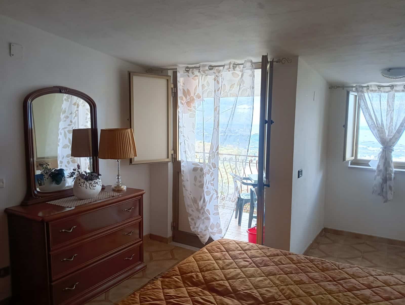 Camere da letto con balcone vista mare, arredamento accogliente e luce naturale, ideale per soggiorni rilassanti. La stanza presenta mobili in legno, tende leggere e un letto in tessuto caldo, perfetti per creare un’atmosfera confortevole.