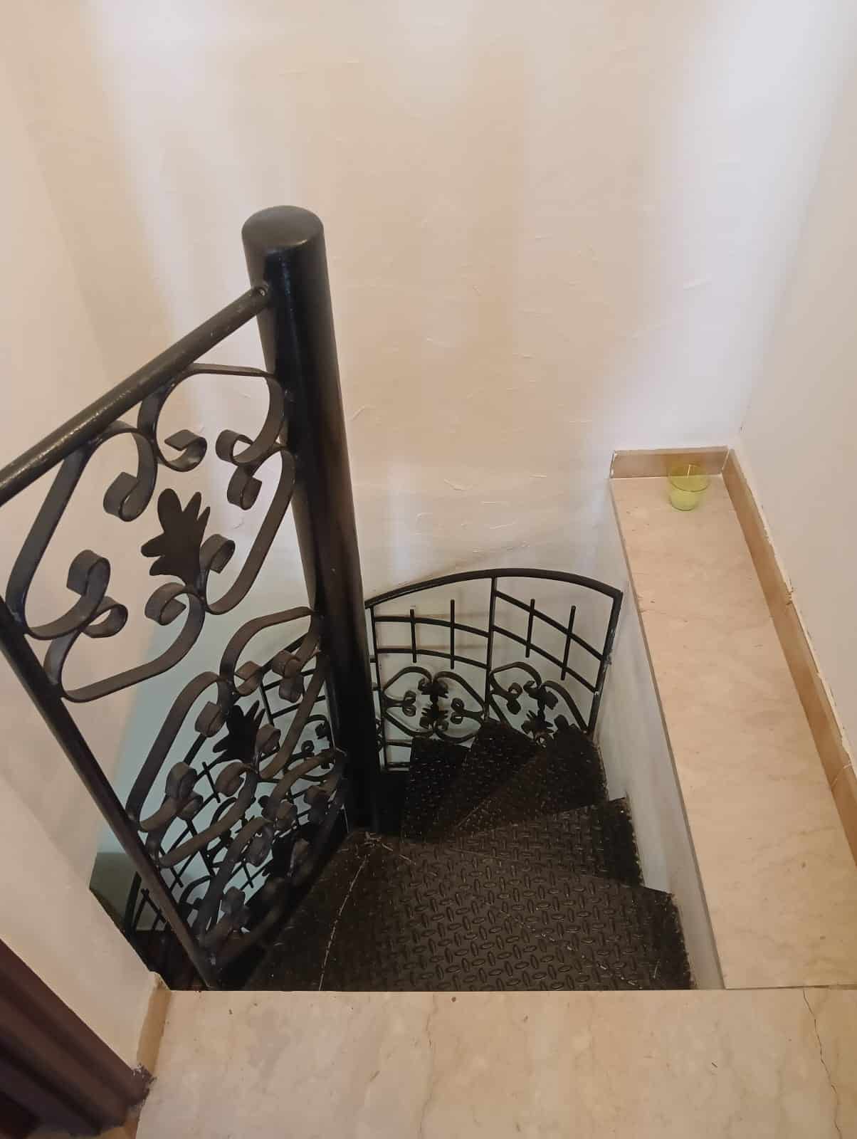 Frare in ferro battuto per scale interne, decorativo e resistente, installato in un edificio residenziale, con pavimento in marmo chiaro e pareti bianche.