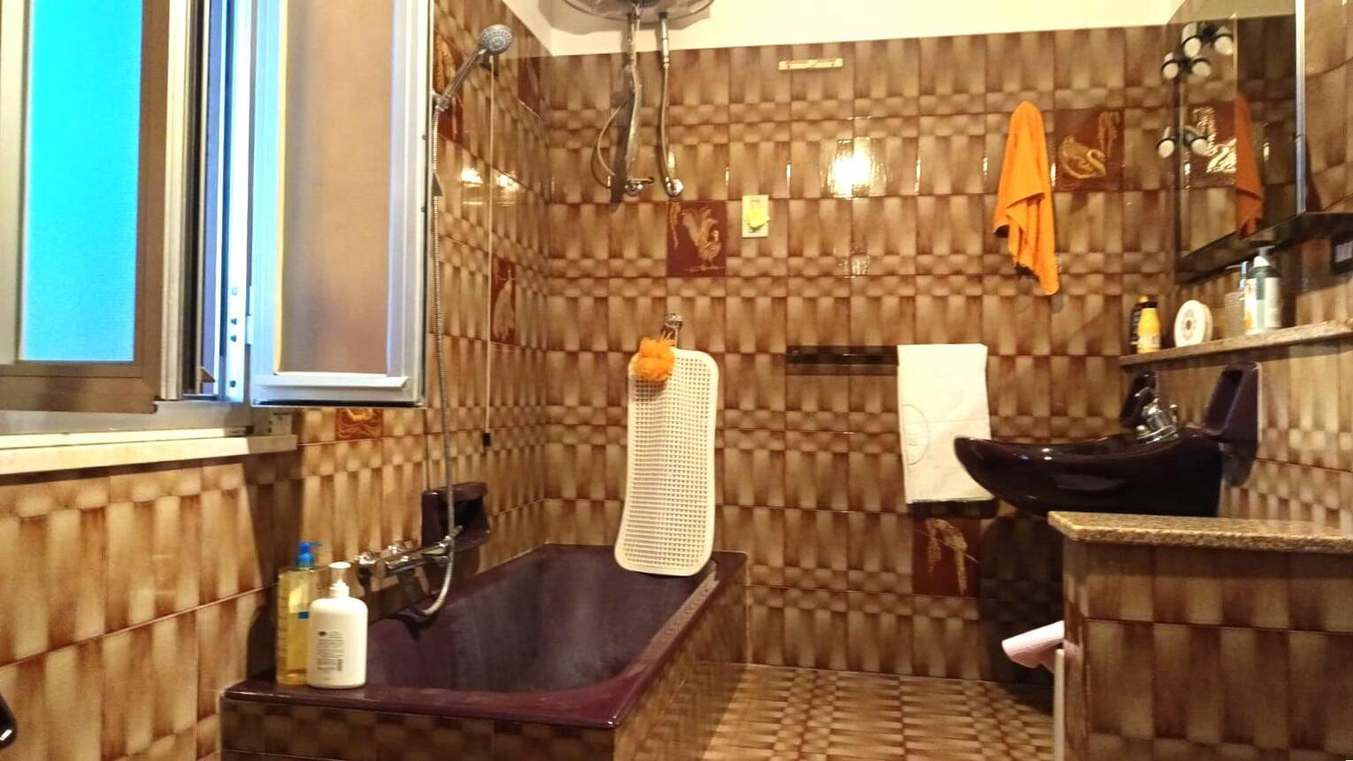 Bagno rustico con piastrelle in tonalità marrone, vasca idromassaggio, soffitto alto e dettagli in legno, specchi e accessori bagno; stile caldo e accogliente.