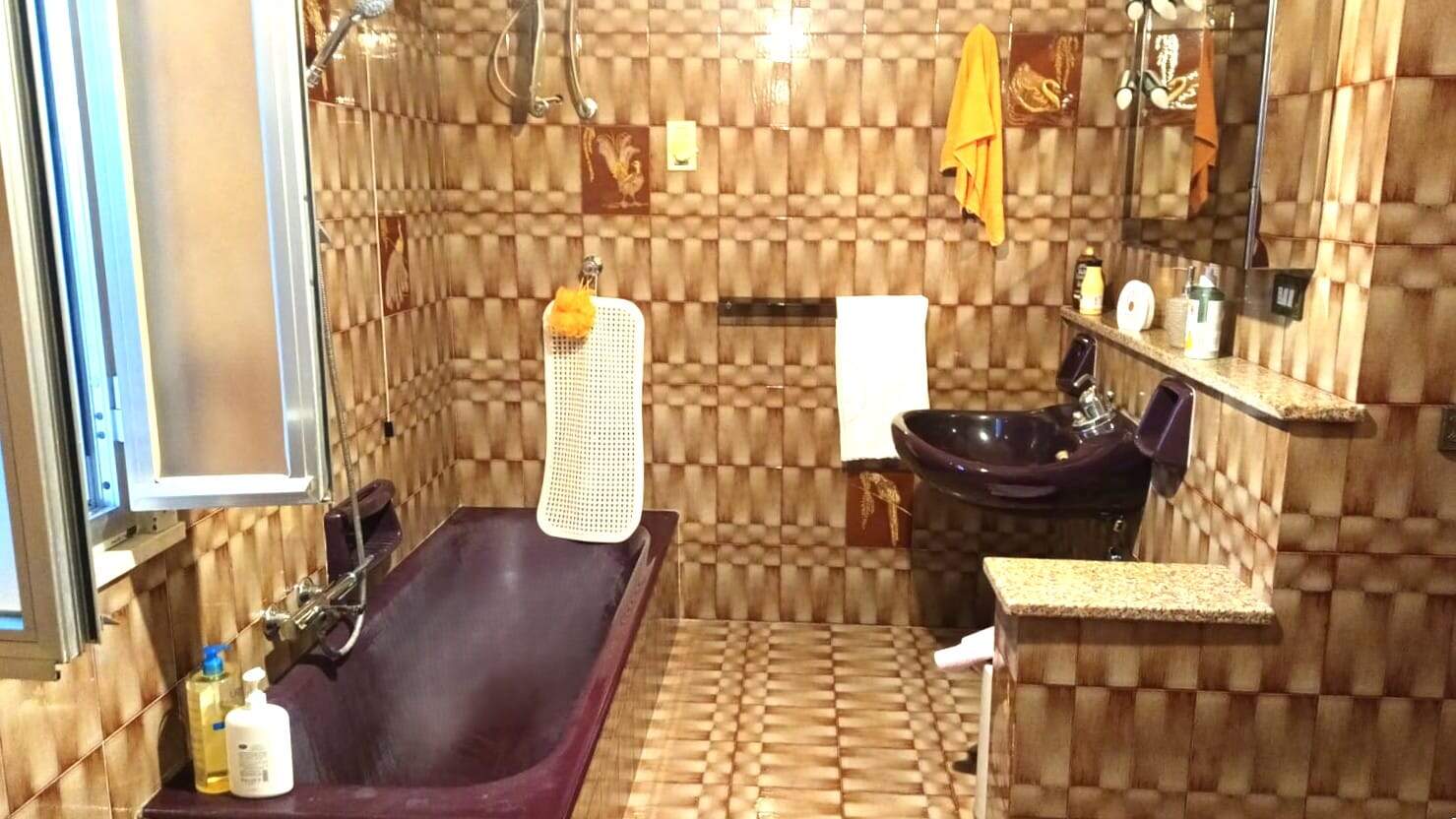 Lavabo nero e vasca da bagno in bagno con pareti e pavimenti in ceramica marrone 3D, asciugamani arancioni, esposizione alla finestra, accessori per il bagno, decorazioni colorate.