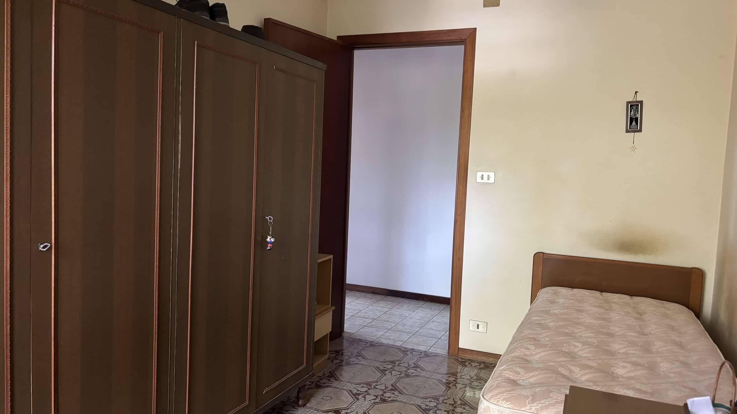 Armadio in legno scuro camera da letto, stanza con letto singolo e ingresso in corridoio, stile semplice, arredamento funzionale, ambiente domestico.