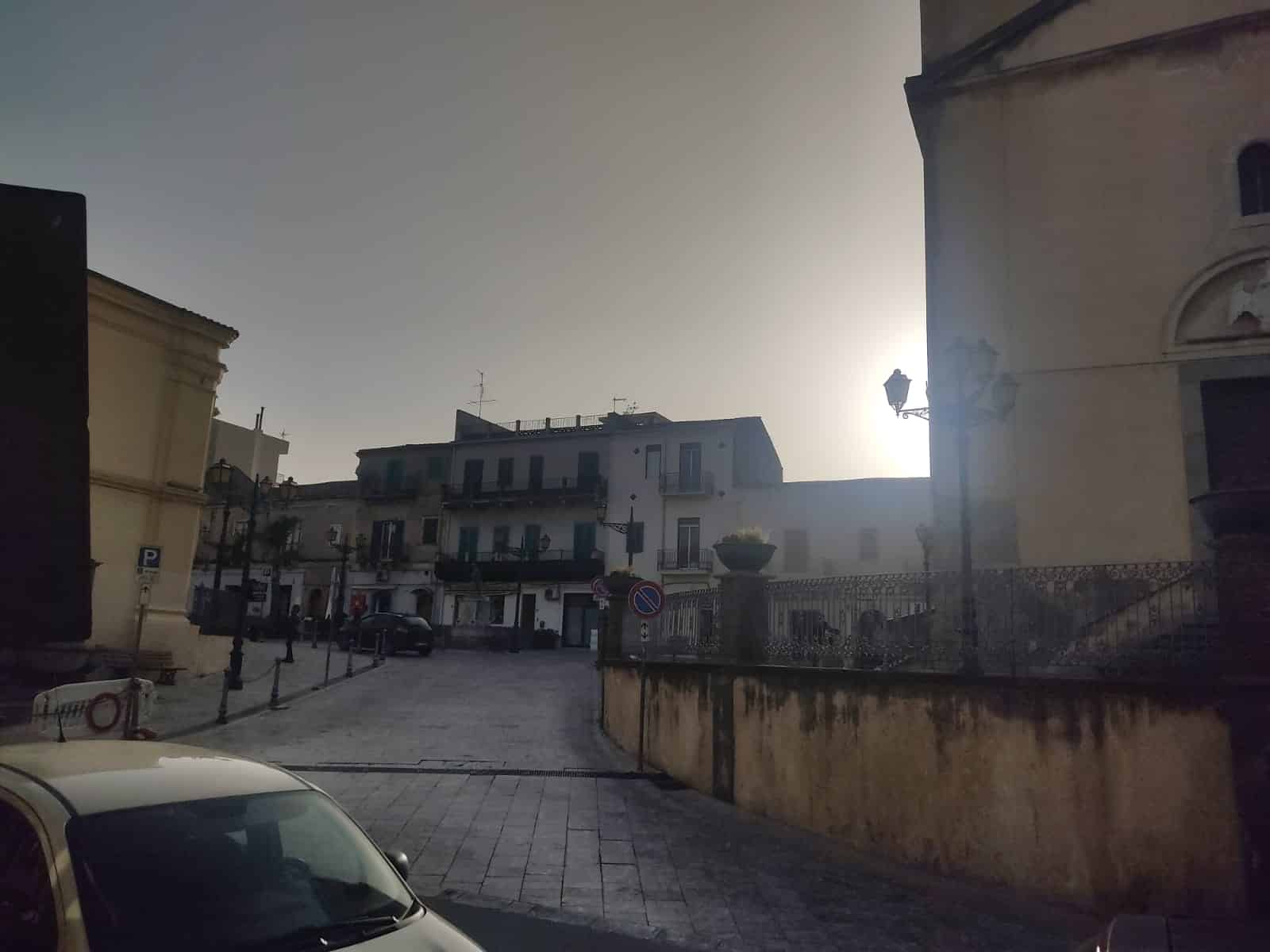 Vicolo di una piazza storica con edifici residenziali e lampioni eleganti, tramonto all'orizzonte, atmosfera tranquilla e autentica città italiana.