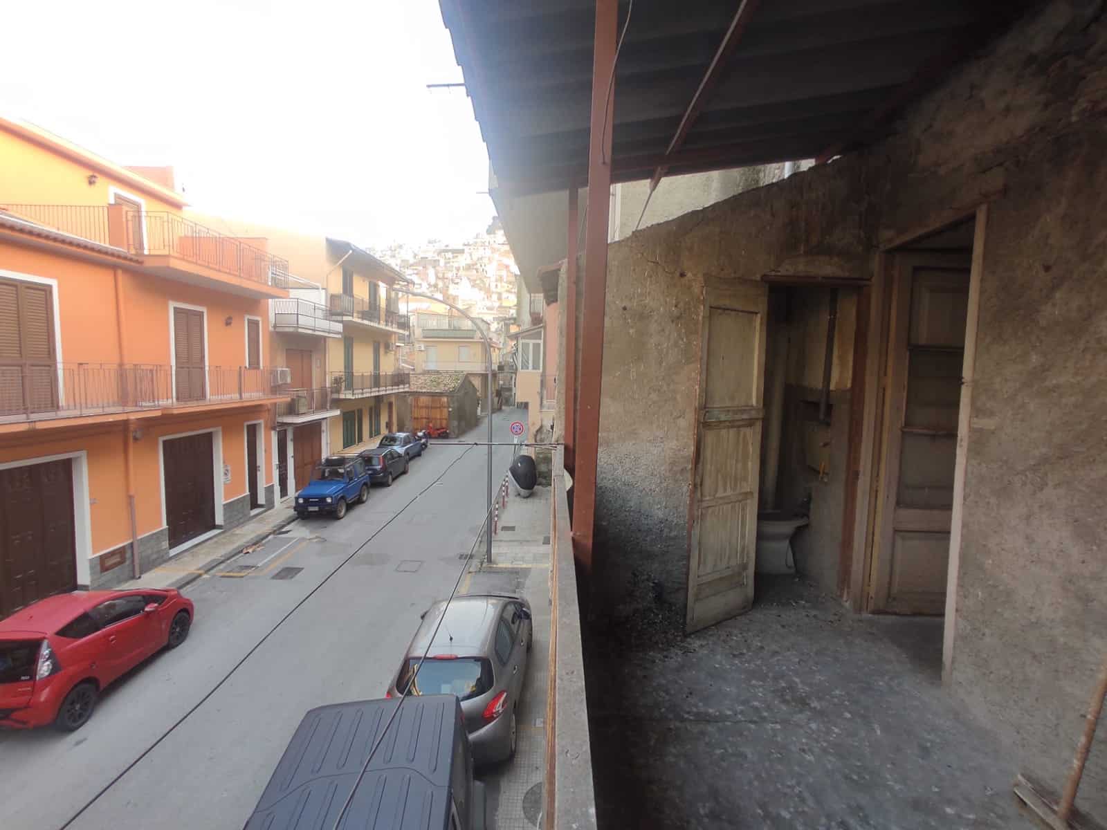 Vecchio balcone in pietra con ripostiglio e servizi igienici, vista sulle case colorate di un quartiere caratteristico di NextCasa, urbanistica storica e autentica.