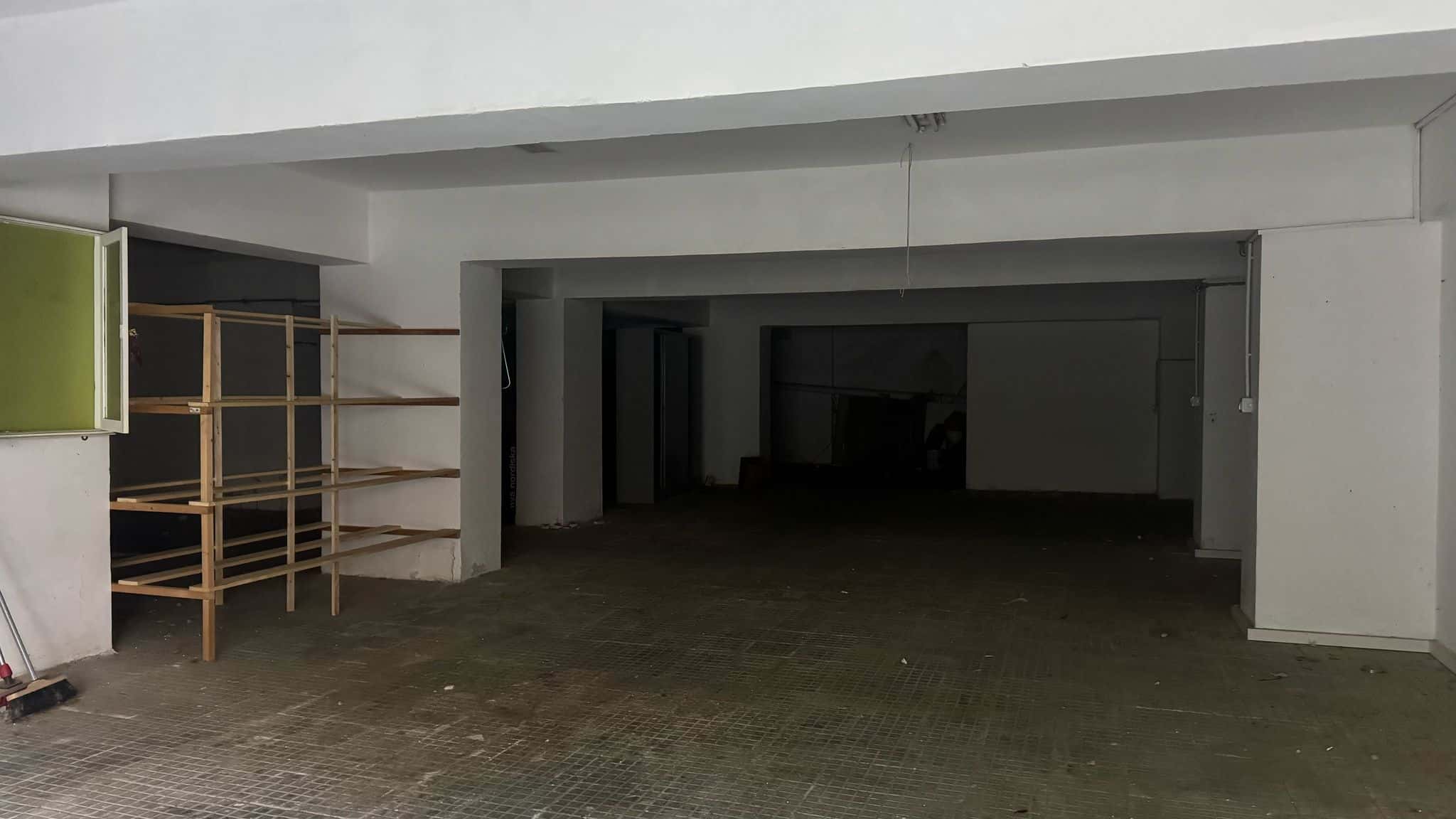 Fondo negozio vuoto con pareti bianche, pavimento in piastrelle e scaffalature in legno, pronto per allestimento commerciale a Milano.