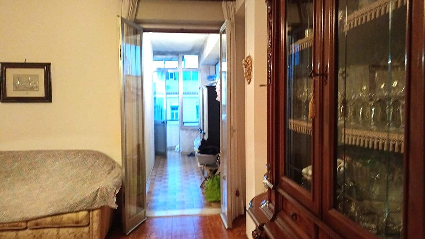 Immagine di un soggiorno con mobile anticato e cucina a vista, illuminato dall'illuminazione naturale, con vista sulla balconata che dà su un edificio residenziale.