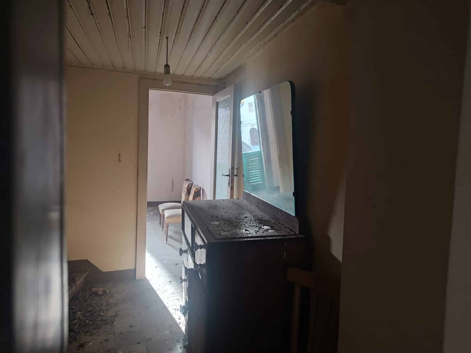 Vecchia cucina in rovina con mobili mancanti e sporchi, luce naturale che entra attraverso la porta finestra che apre su un balcone.