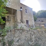 Vecchio edificio rustico su collina con scale in pietra, muri in pietra e legno, vegetazione circostante, scenario naturale e rurale.