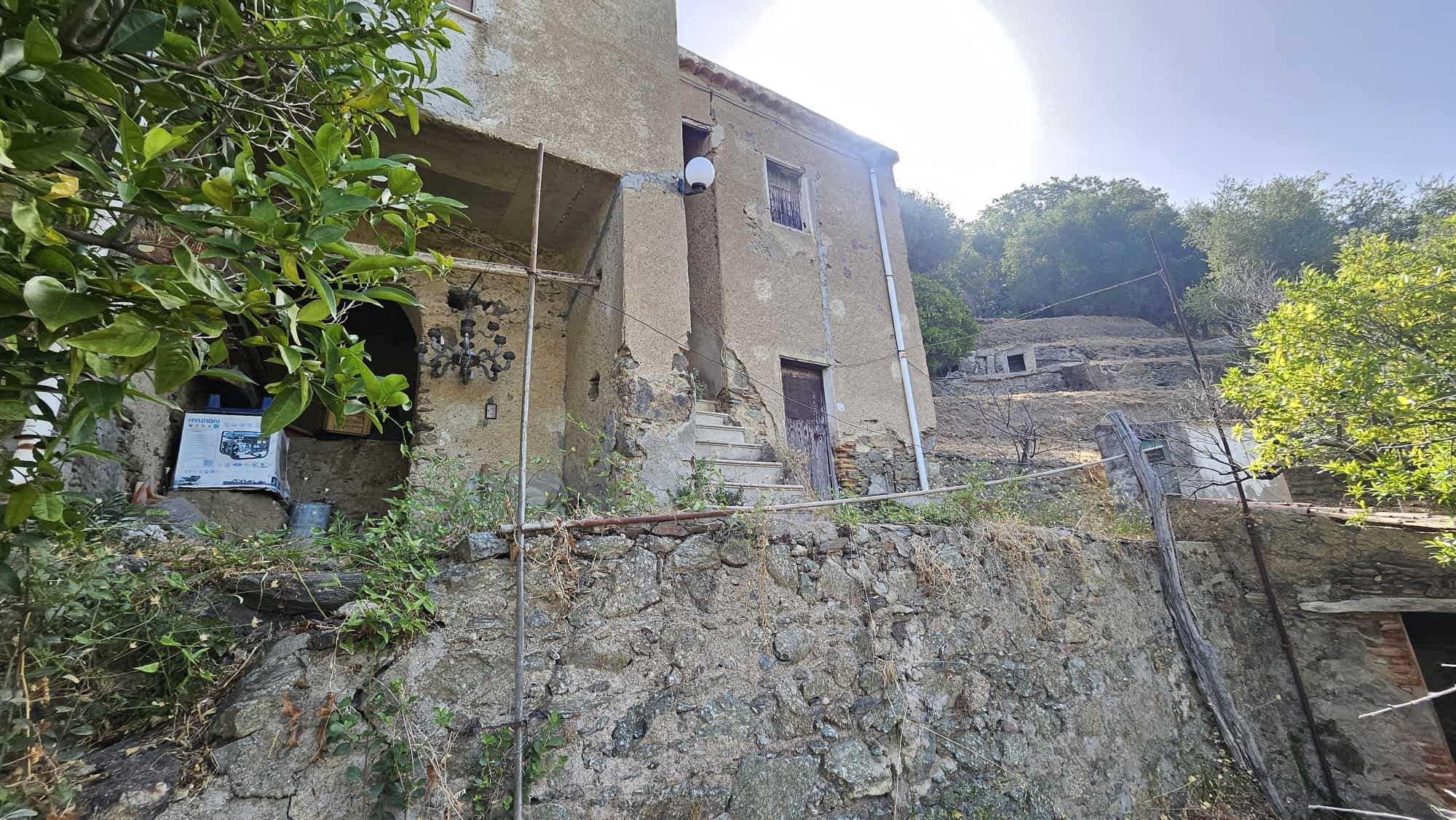 Vecchio edificio rustico su collina con scale in pietra, muri in pietra e legno, vegetazione circostante, scenario naturale e rurale.