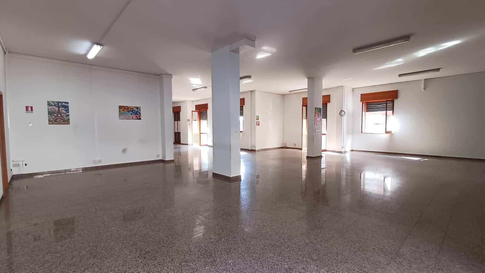 Ampio spazio commerciale vuoto con pareti bianche, grandi finestre e illuminazione a LED, ideale per ufficio o boutique, pavimento in granito e ambienti luminosi.