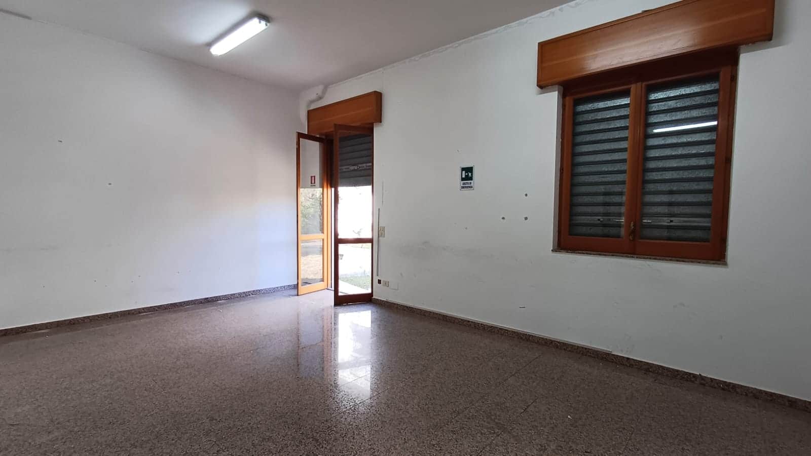 Locale senza arredi con pareti bianche, finestra con tapparelle e porta d'ingresso con vetrata, pavimento in gres, ideale per rinnovare e personalizzare la casa.