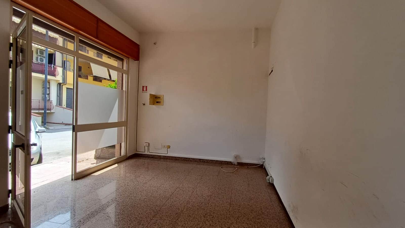 Finestra e porta di ingresso in un negozio vuoto con pavimento in marmo, pareti bianche e spazio per attività commerciali, in un contesto urbano.