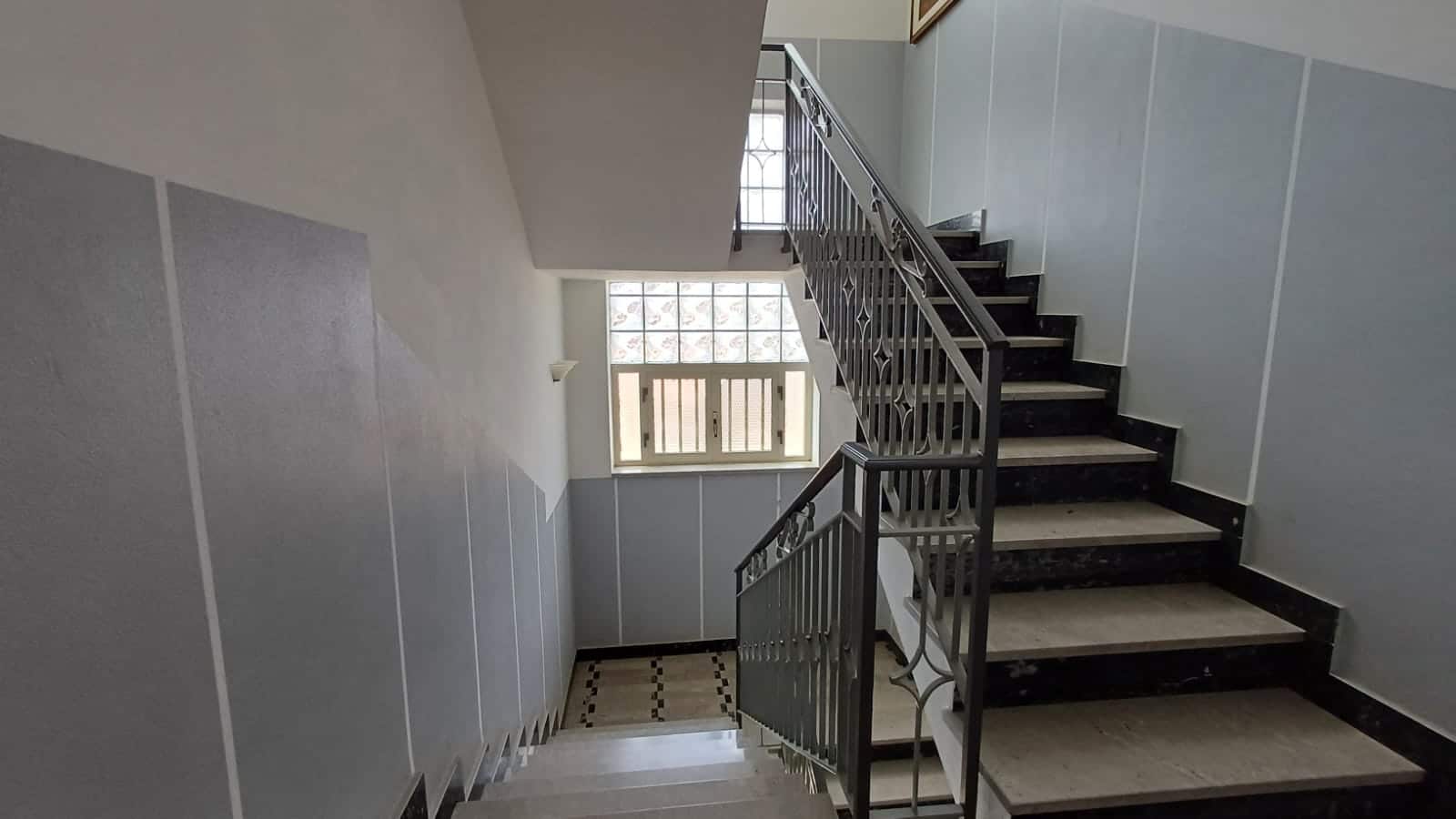 Scala interna di edificio residenziale con ringhiera in metallo, luce naturale dalle finestre, ambiente luminoso e spazioso, ideale per immagini di immobili residenziali su NextCasa.