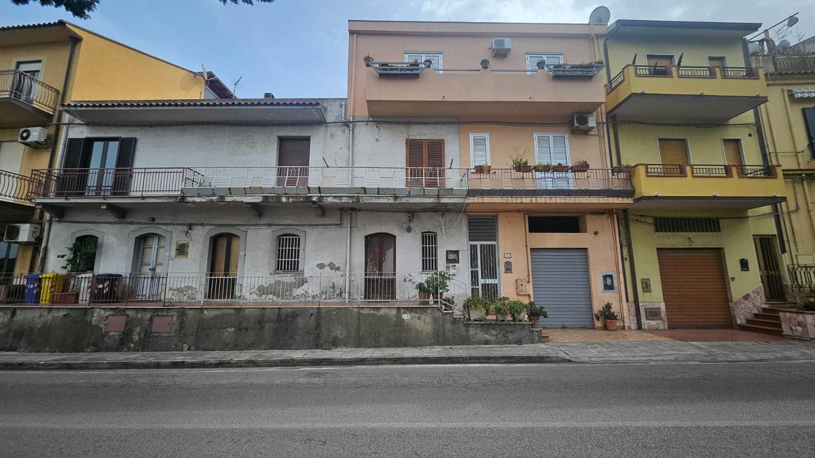 Vecchio edificio residenziale multifamiliare in via urbana, con balconi e finiture estetiche variate, lungo strada trafficata, mostrando stato di manutenzione parziale e dettagli architettonici degli appartamenti.