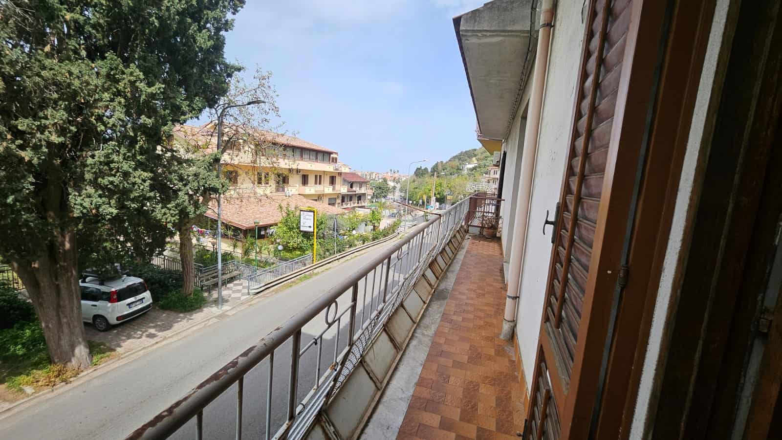 Balcone di un appartamento con vista su strada e natura, ideale per living all'aperto, immerso nel contesto urbano e residenziale.