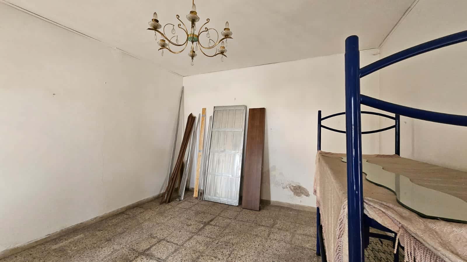 Rustico da ristrutturare con soffitto con lampadario e pavimento in piastrelle, armadio, porta in legno e struttura letto a castello in colore blu. Ideale per investimento immobiliare o casa da personalizzare.