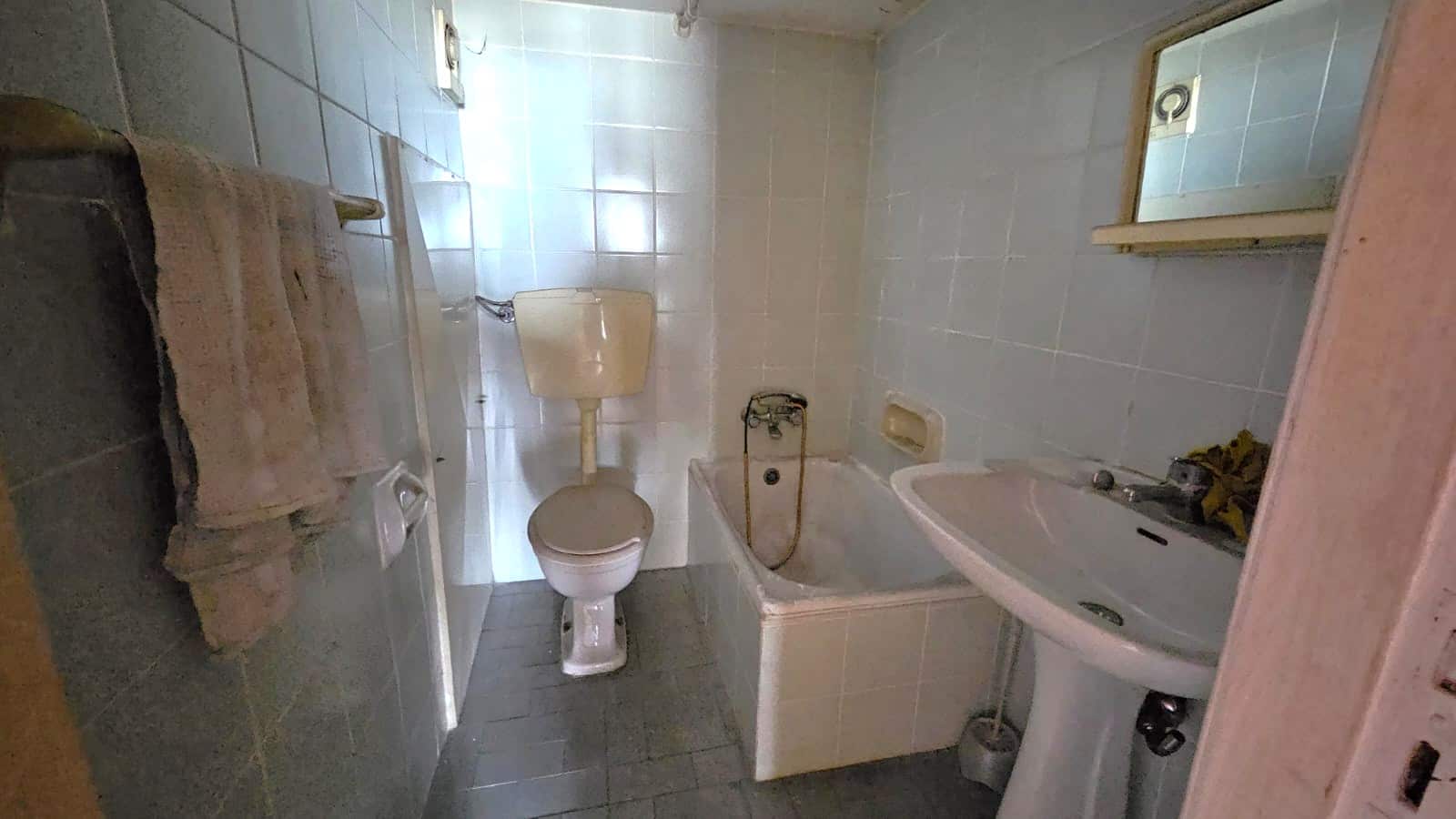 Bagno con piastrelle bianche e vasca da bagno usata in vendita. Lavandino, specchio, WC e dettagli di ristrutturazione parziale. Ideale per ristrutturare o rinnovare.