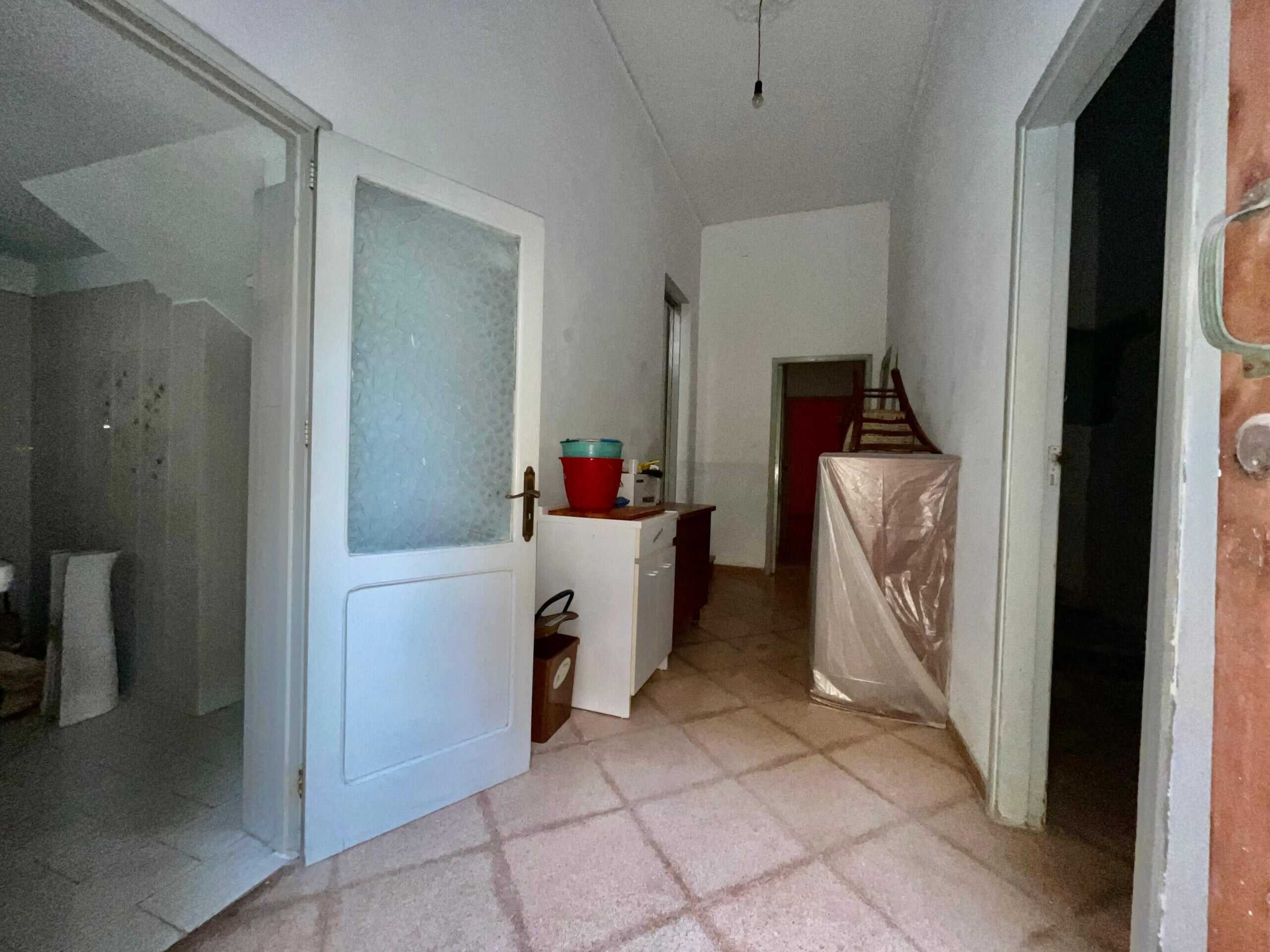 Vecchio ingresso e corridoio interno di casa in ristrutturazione con pavimento in piastrelle beige e porte bianche. Spazi da rinnovare, ideale per progetto di ristrutturazione immobiliare.