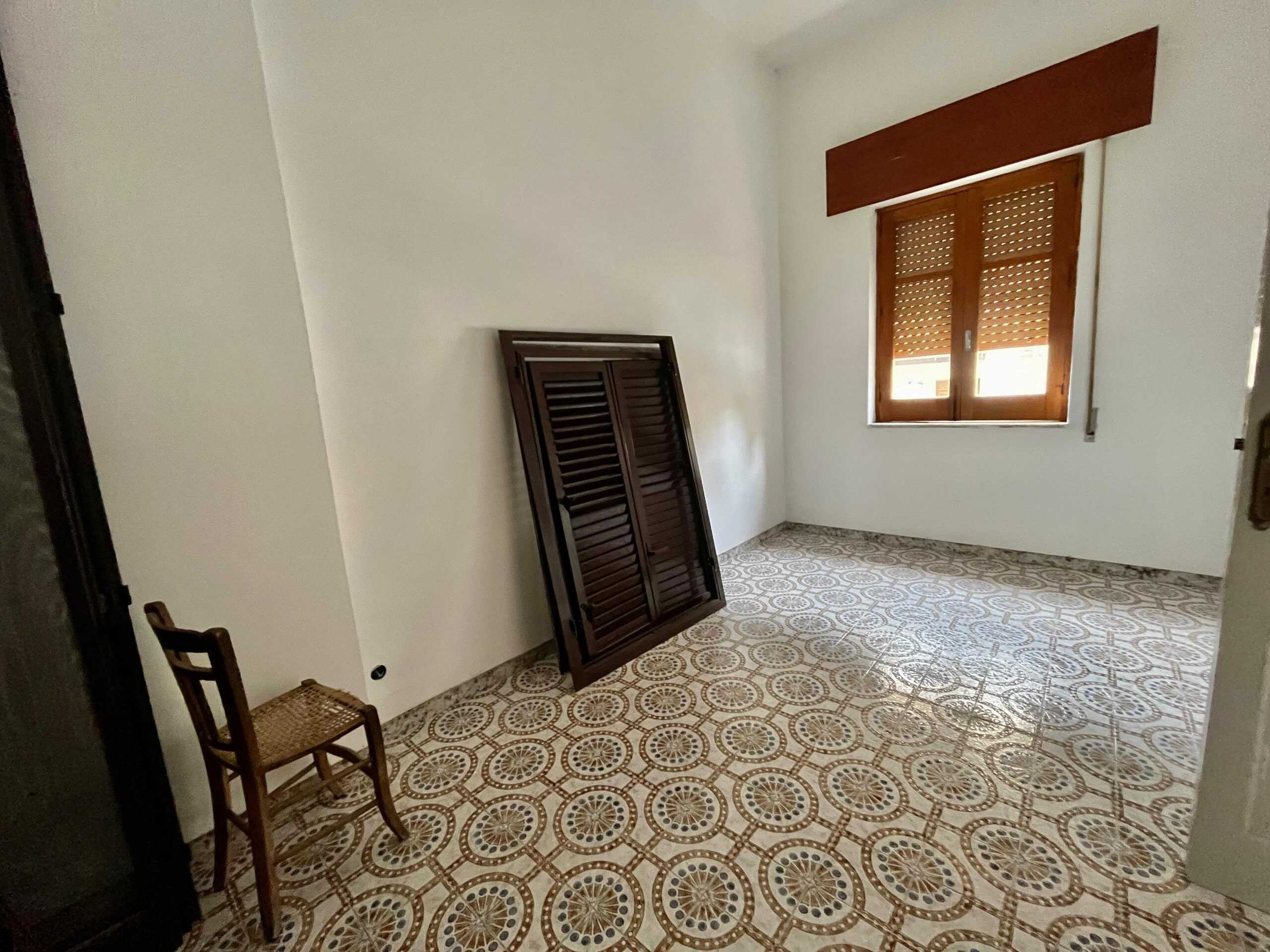 Immagine WhatsApp 2025-03-24 ore 10.41.06_ffd6c8a8 Stanza vuota in affitto con pareti bianche, finestra in legno con persiane e pavimento in piastrelle decorative, ideale per soluzioni abitative o ufficio.