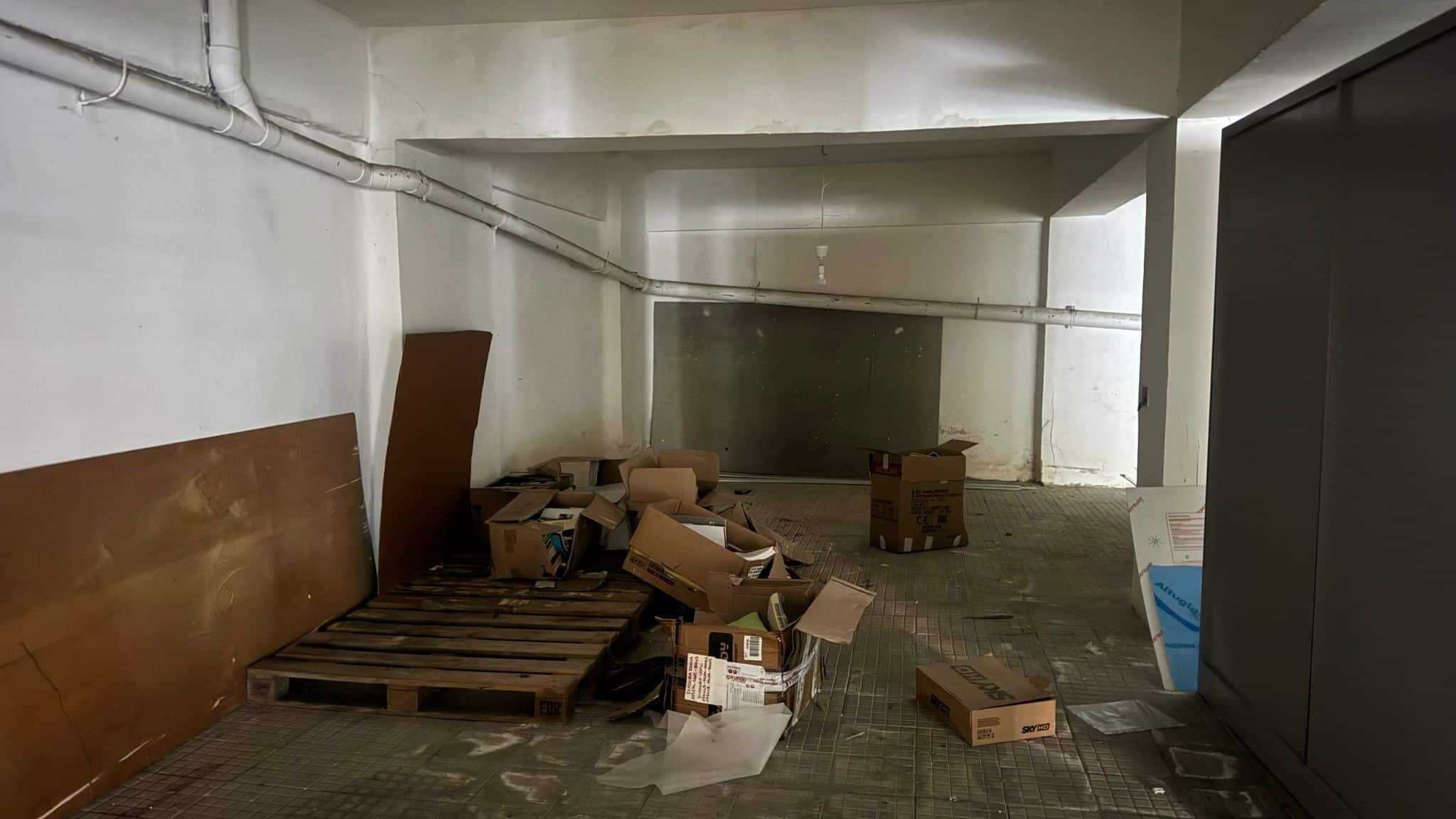 Scaffali e scatole di immondizia in un garage o magazzino trascurato e disordinato con pavimento in piastrelle e pareti bianche.