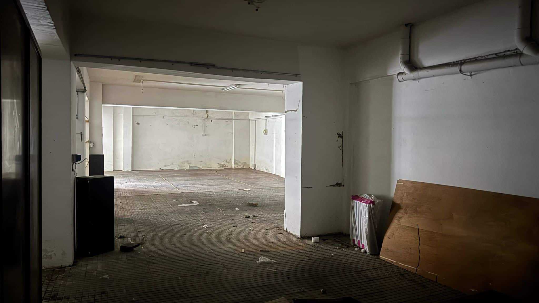 Magazzino in affitto con spazio commerciale, soffitto alto, muri bianchi, pavimento in piastrelle rustiche, ideale per attività di stoccaggio o showroom. Ambiente luminoso e versatile, pronto per ristrutturazione.