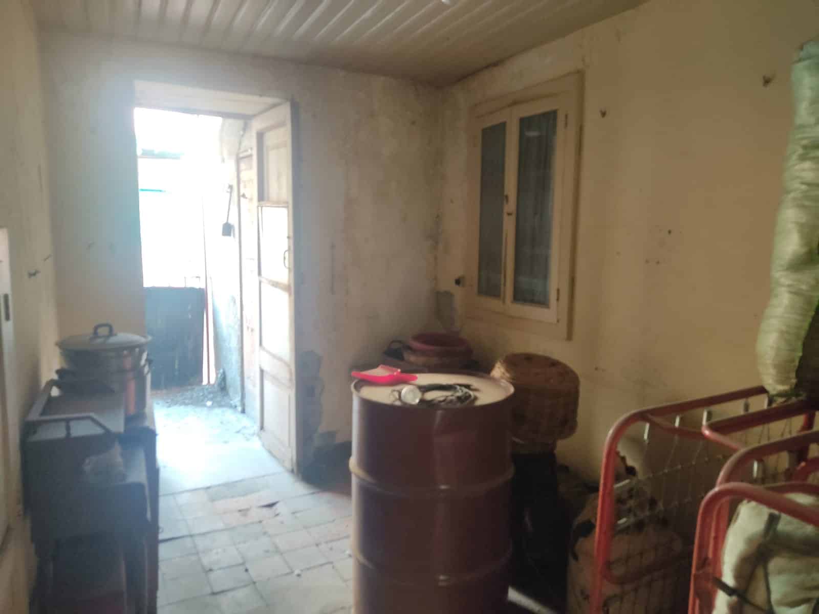 Deposito rustico con porta di accesso, pareti in pietra, finestra e arredi vari per il deposito. Ideale per conservare attrezzi e oggetti in un ambiente tradizionale e funzionale.
