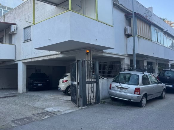 Ampio parcheggio sotto edificio residenziale a Napoli, con diverse auto parcheggiate, ingresso con cancello in ferro e zona garage coperta, in zona tranquilla e ben servita.