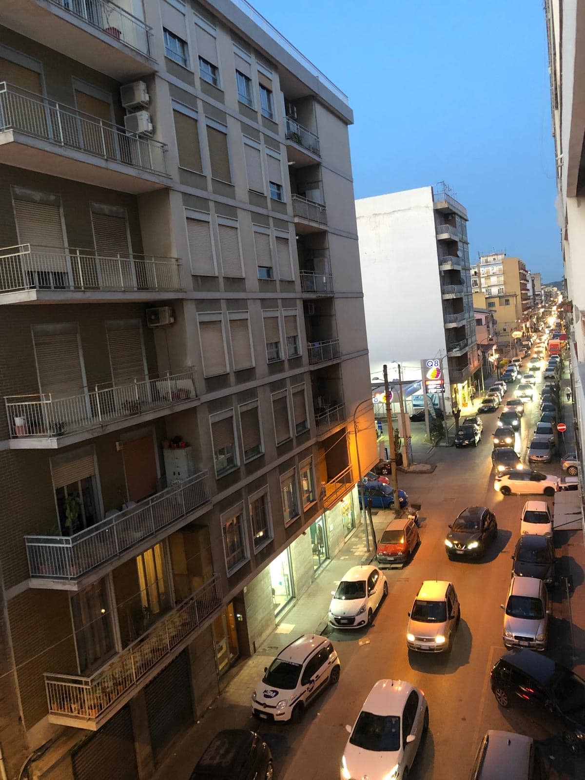 Finestra sulla strada di una città con edifici alti, veicoli parcheggiati e luci serali, rappresenta un ambiente urbano e moderno e il quotidiano stile di vita in una zona residenziale.