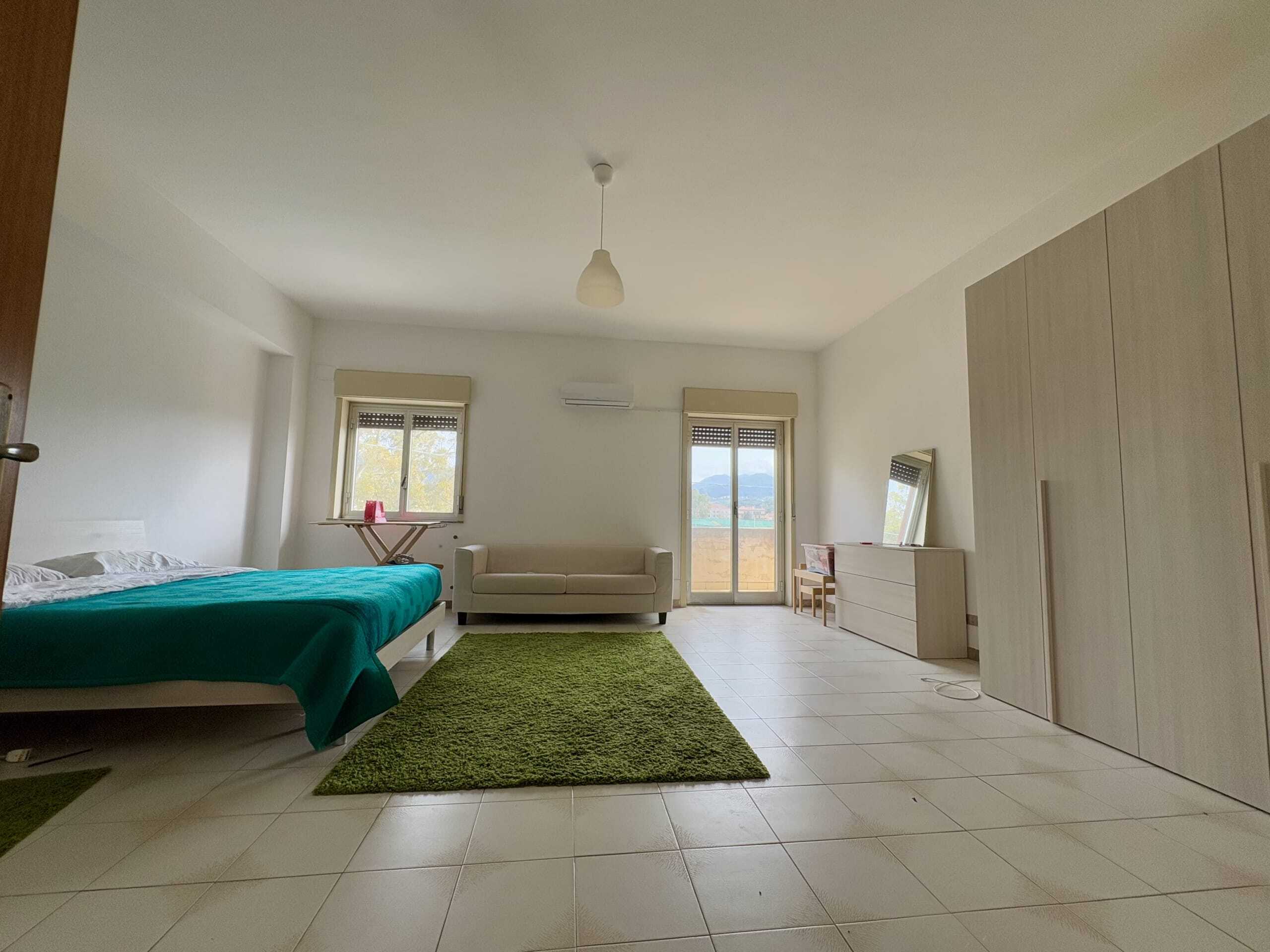 Camera da letto spaziosa e luminosa con letti comodi, divano e grande armadio, affacciata su un terrazzo con vista sul verde, ambiente elegante e ben arredato, ideale per residenze moderne a Napoli.
