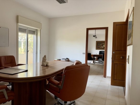 Sala riunioni moderna e luminosa con grandi finestre, tavolo in legno, sedie ergonomiche in pelle color caramello, ambiente professionale adatto per incontri di lavoro e conferenze.