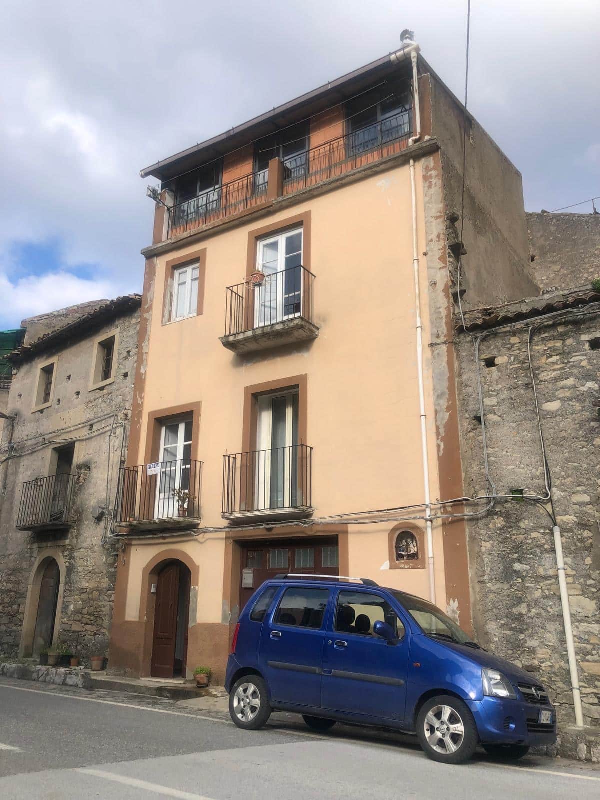 Affaccio su edificio storico ristrutturato con balconi e pareti in tonalità calde, parcheggio auto blu e strada in primo piano.