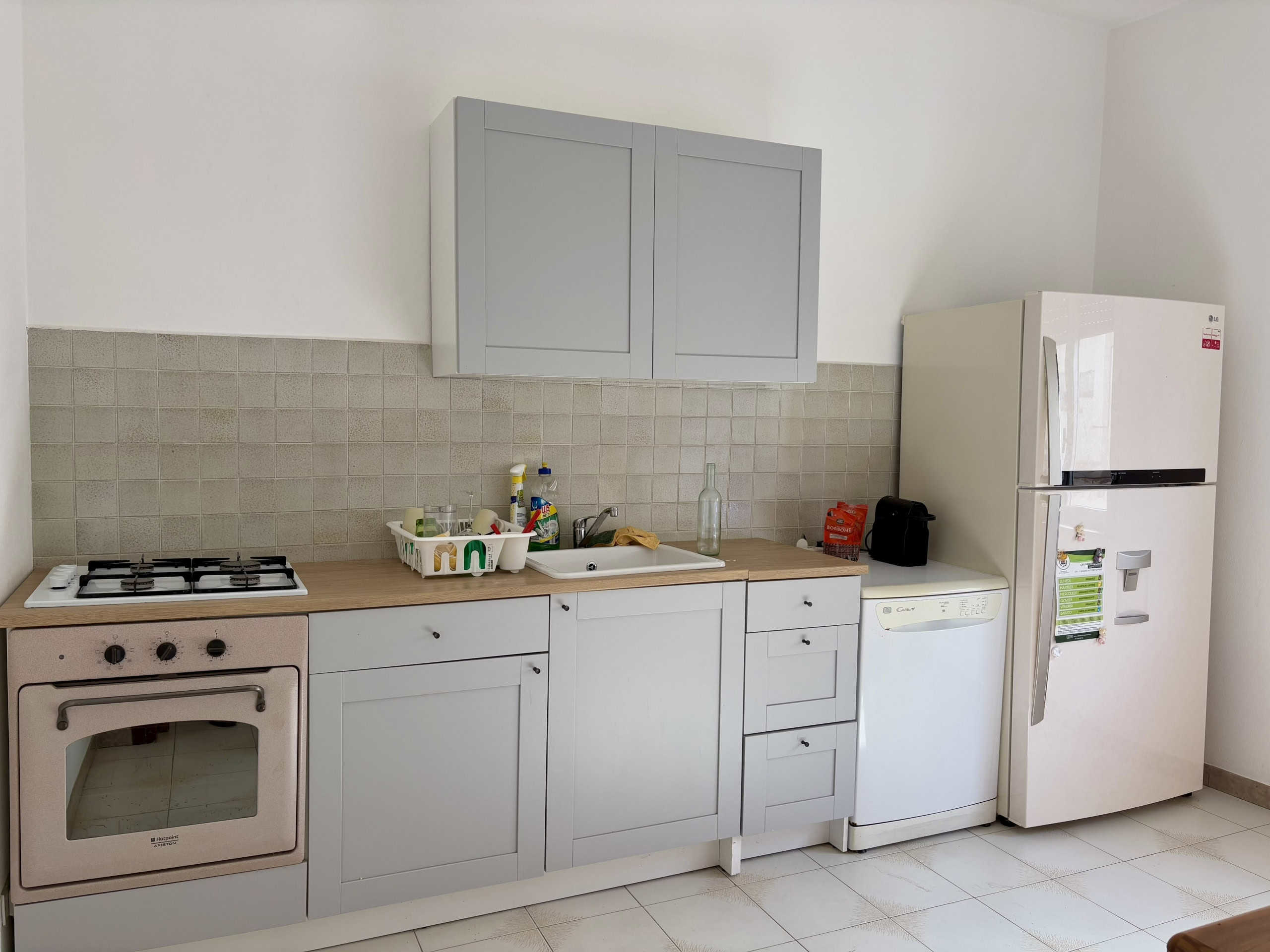 Lavanderia moderna con cucina semplice, frigorifero, lavastoviglie e piano cottura a gas, ideale per case o appartamenti in vendita o affitto, stile minimal e funzionale.