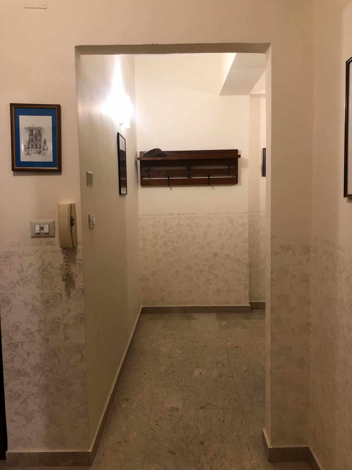 Porta d'ingresso di un appartamento con pareti decorative e mensola in legno, illuminata da una luce calda, spazio elegante e funzionale.
