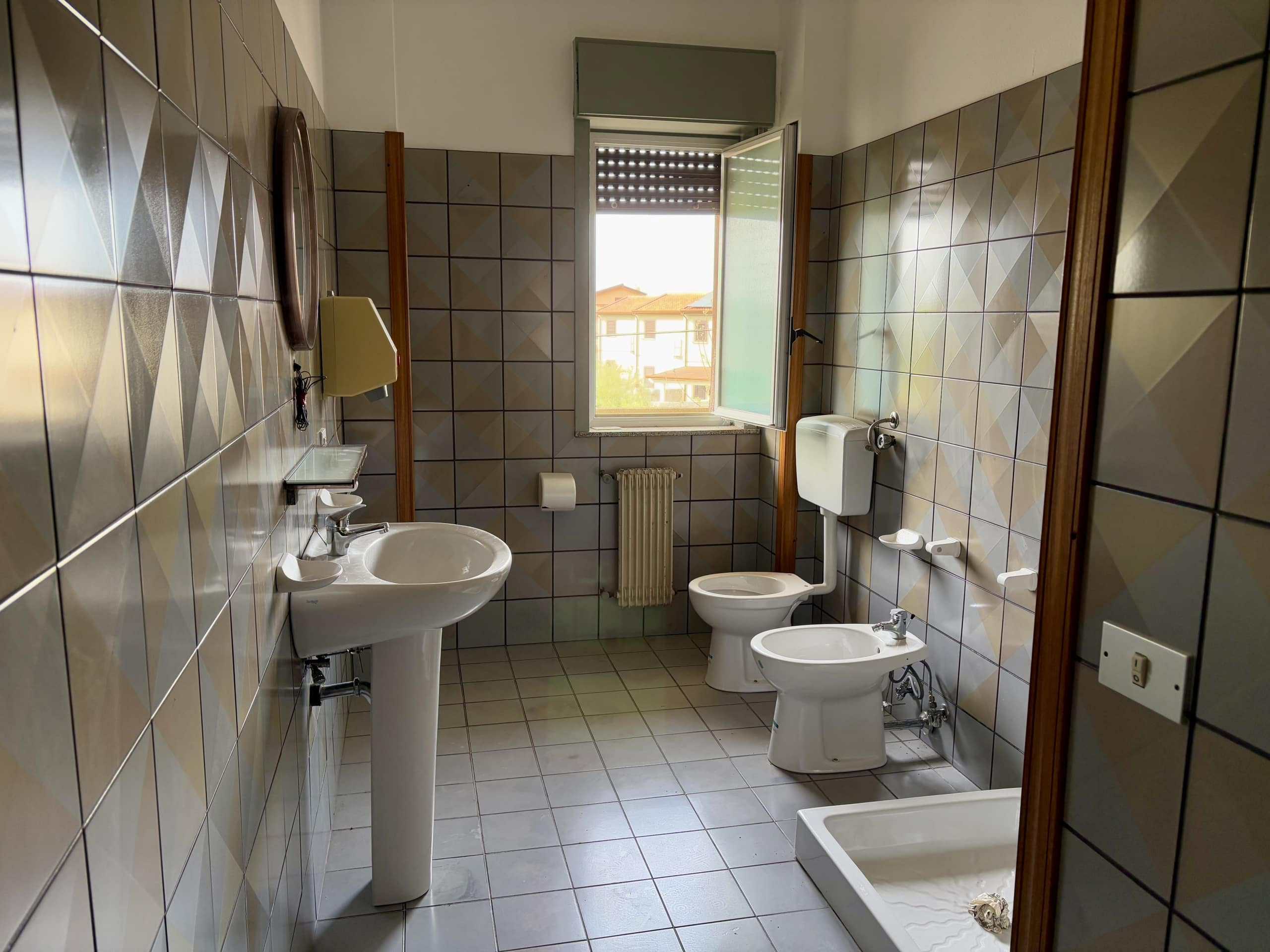 Lavabo e servizi igienici in bagno spazioso con finestra, arredato con piastrelle moderne e funzionali, ideale per soluzioni abitative di qualità.