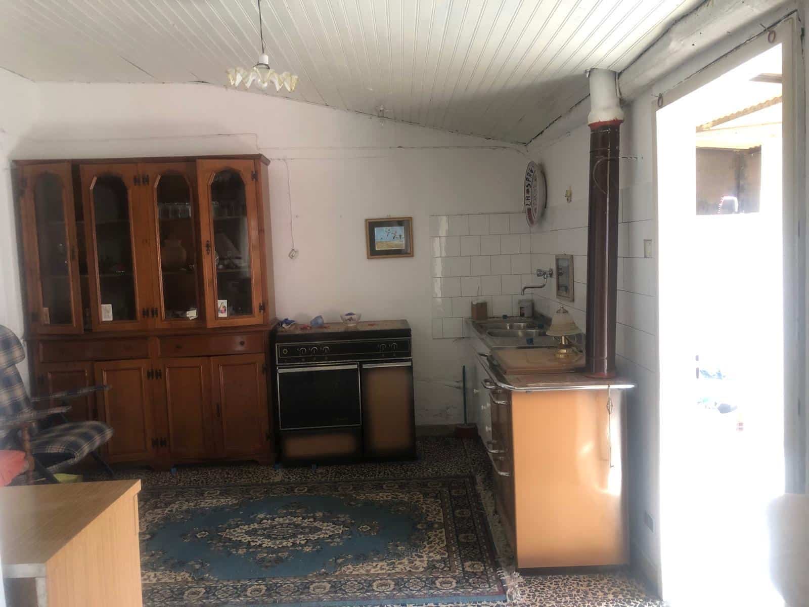 Vecchia cucina rustica con mobile in legno e stufa in stile vintage, pareti bianche e pavimento con tappeto, ambiente semplice e accogliente.
