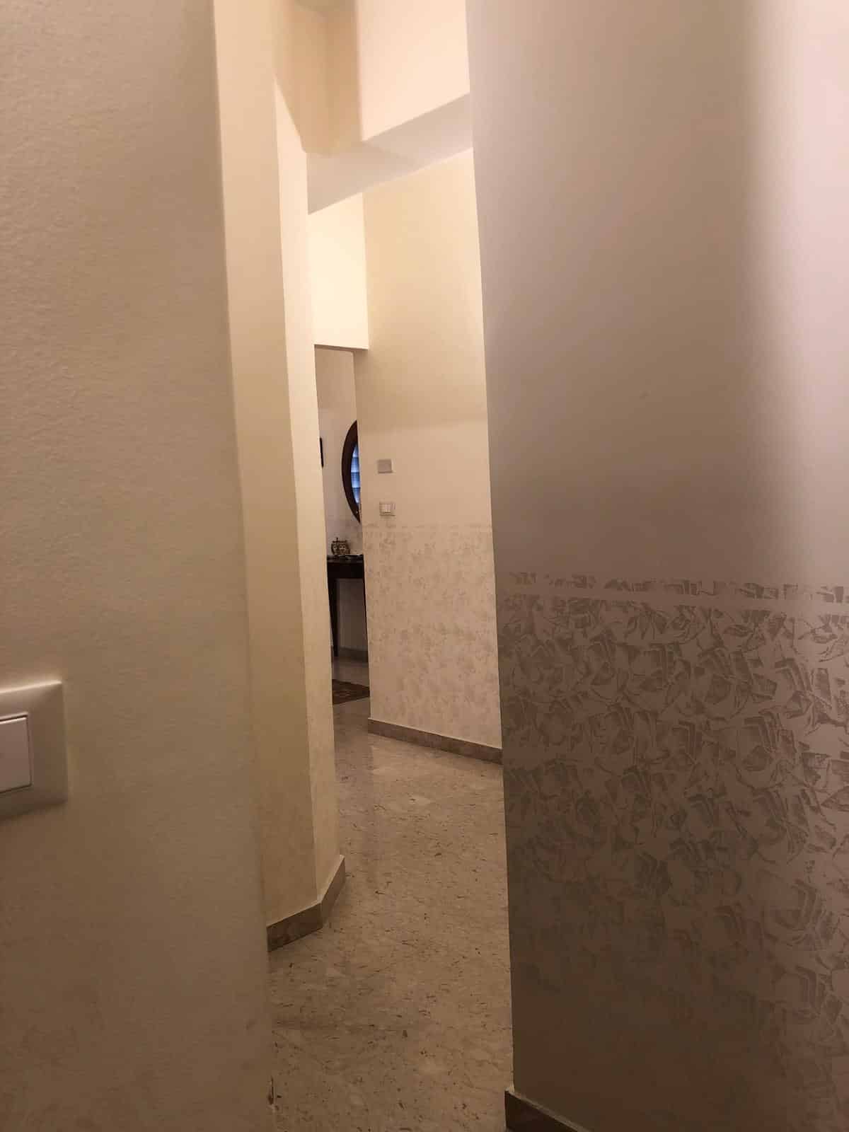 Porta di ingresso in un appartamento moderno con pareti bianche e dettagli decorativi, pavimento in marmo chiaro e illuminazione soffusa per un ambiente accogliente.