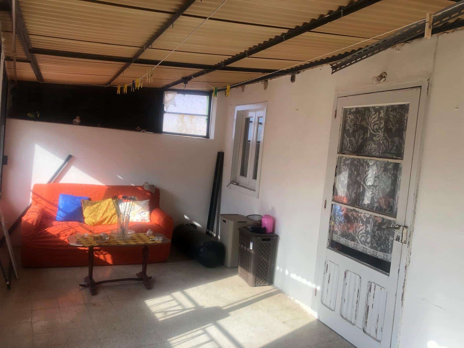 Soggiorno con divano arancione, mobili di legno, finestra luminosa e porta con tende decorative, spazio rustico e accogliente per la casa.