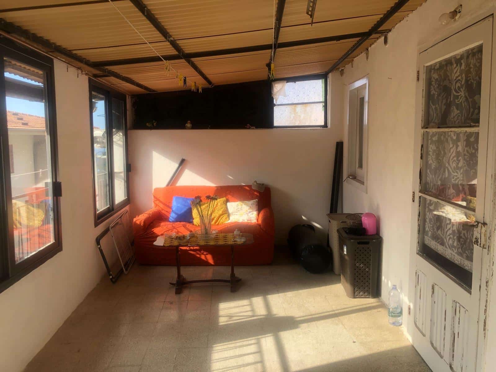 Spazio soggiorno rinnovato con divano arancione, finestre luminose, arredi pratici, porta rustica, zona relax, casa da ristrutturare, ambiente accogliente, elementi di design, clima domestico, ristrutturazione abitativa.
