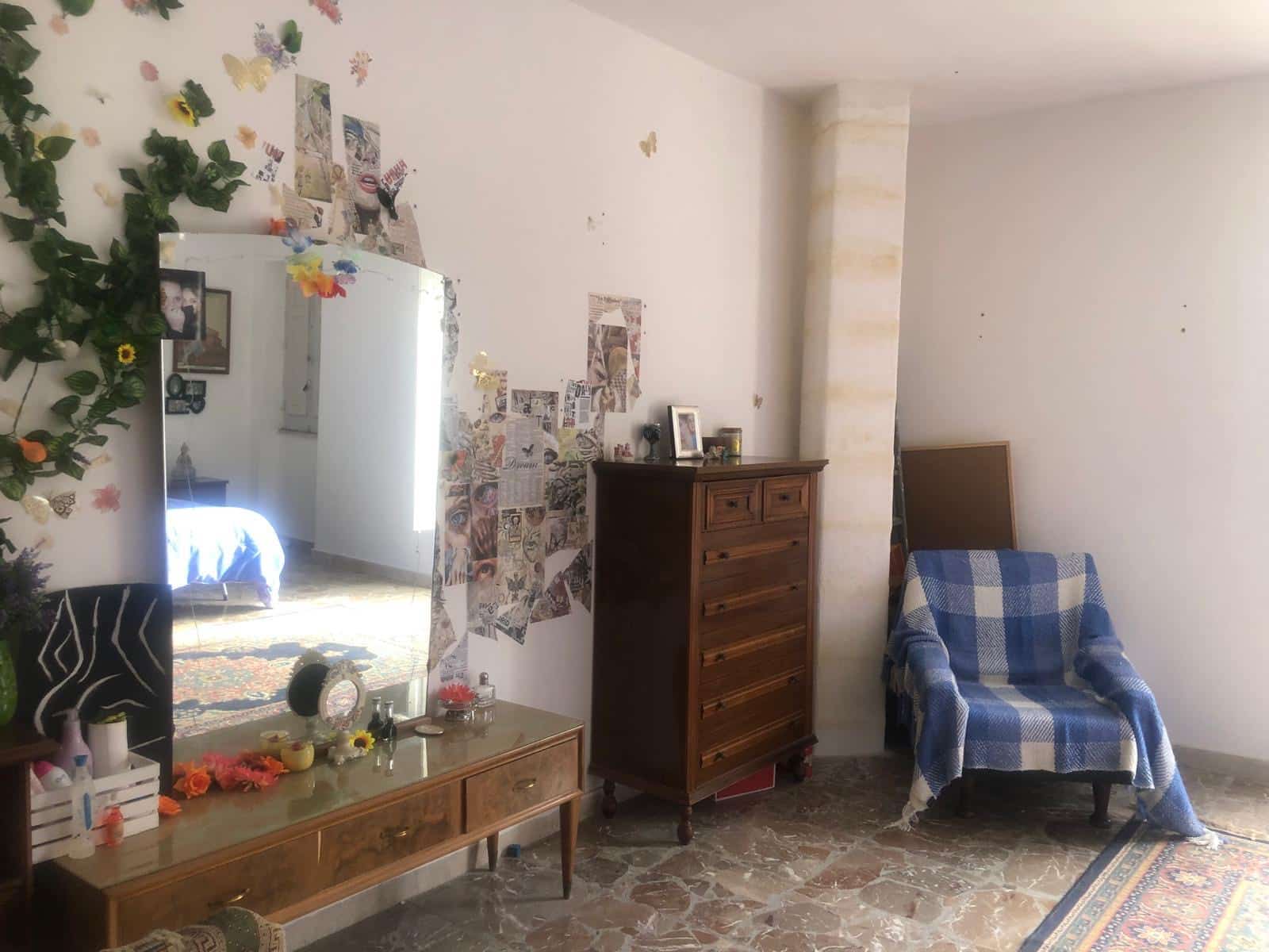 Specchio decorato con collage di immagini e decorazioni floreali, in un ambiente domestico accogliente con mobili in stile vintage, poltrona rivestita con plaid a quadri, ideale per camere da letto o zona giorno.